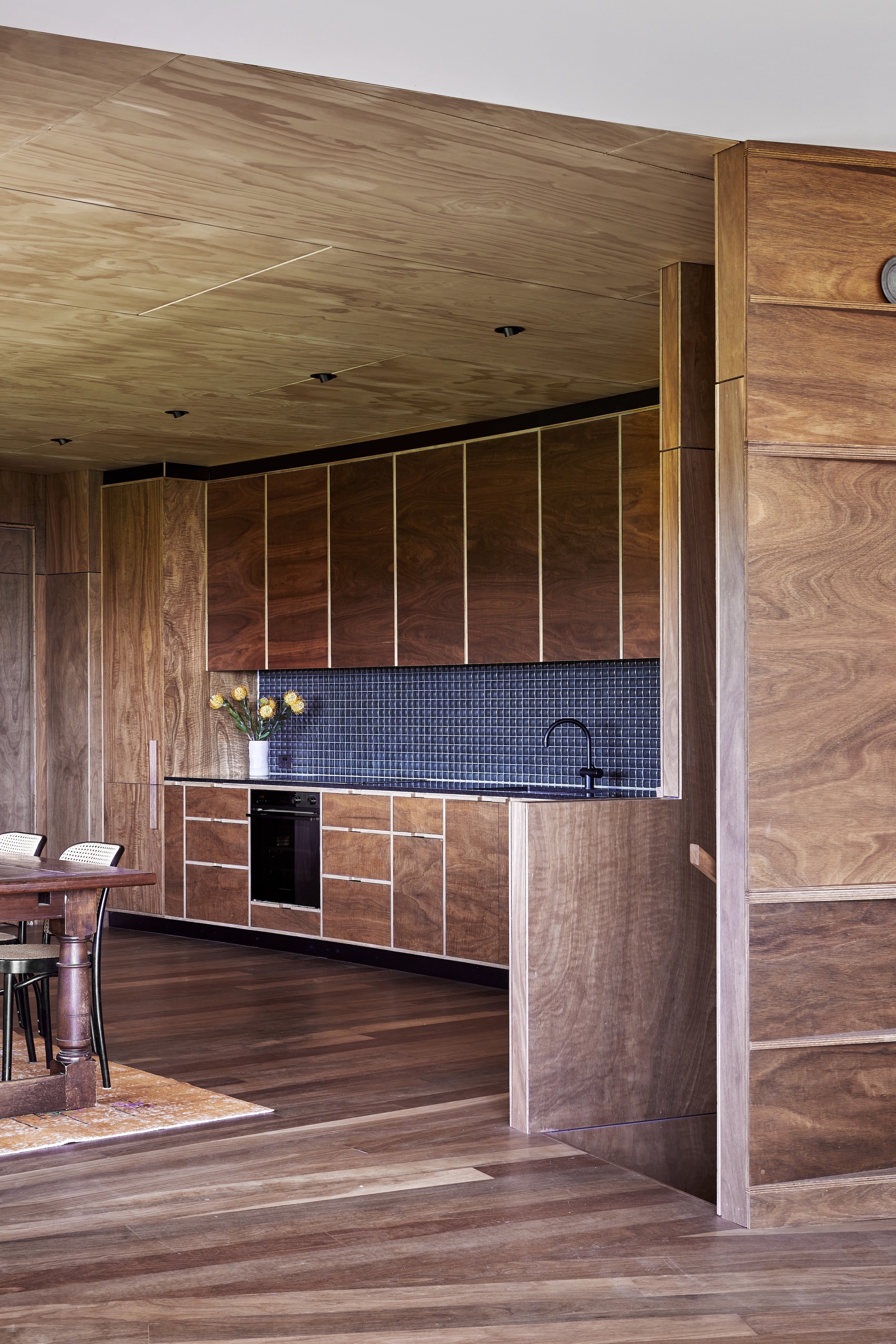 Timber-lined kitchen with dark mosaic tile backsplash and continuous plywood ceiling