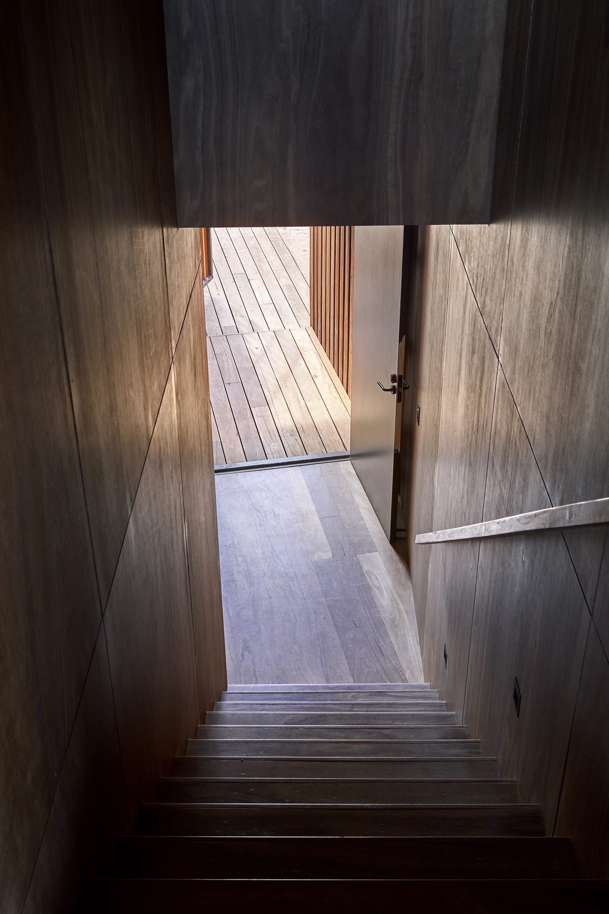 Timber staircase descending toward an open door with afternoon light casting diagonal shadows