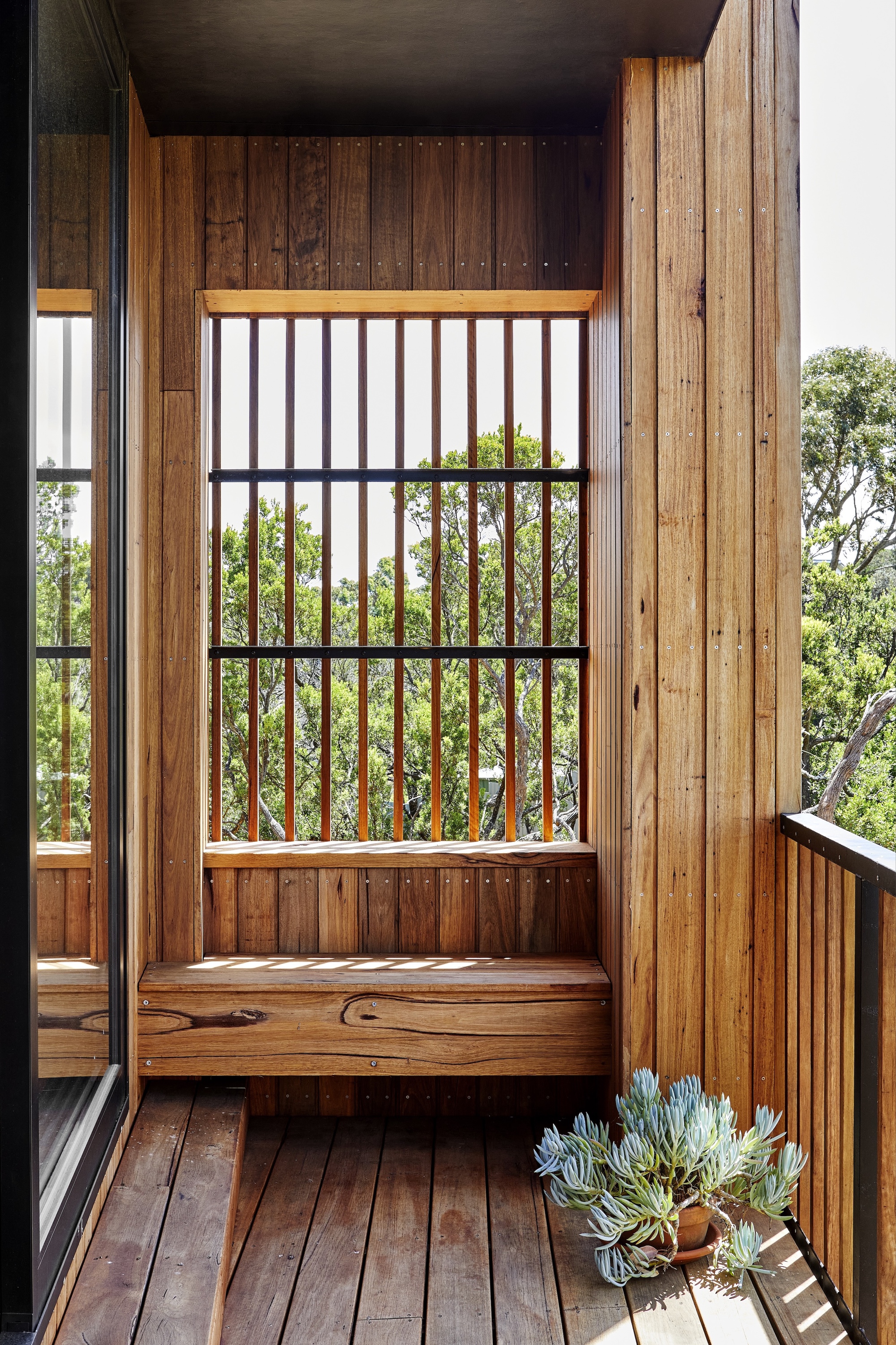 Built-in window seat with vertical timber slat screen framing views of surrounding vegetation
