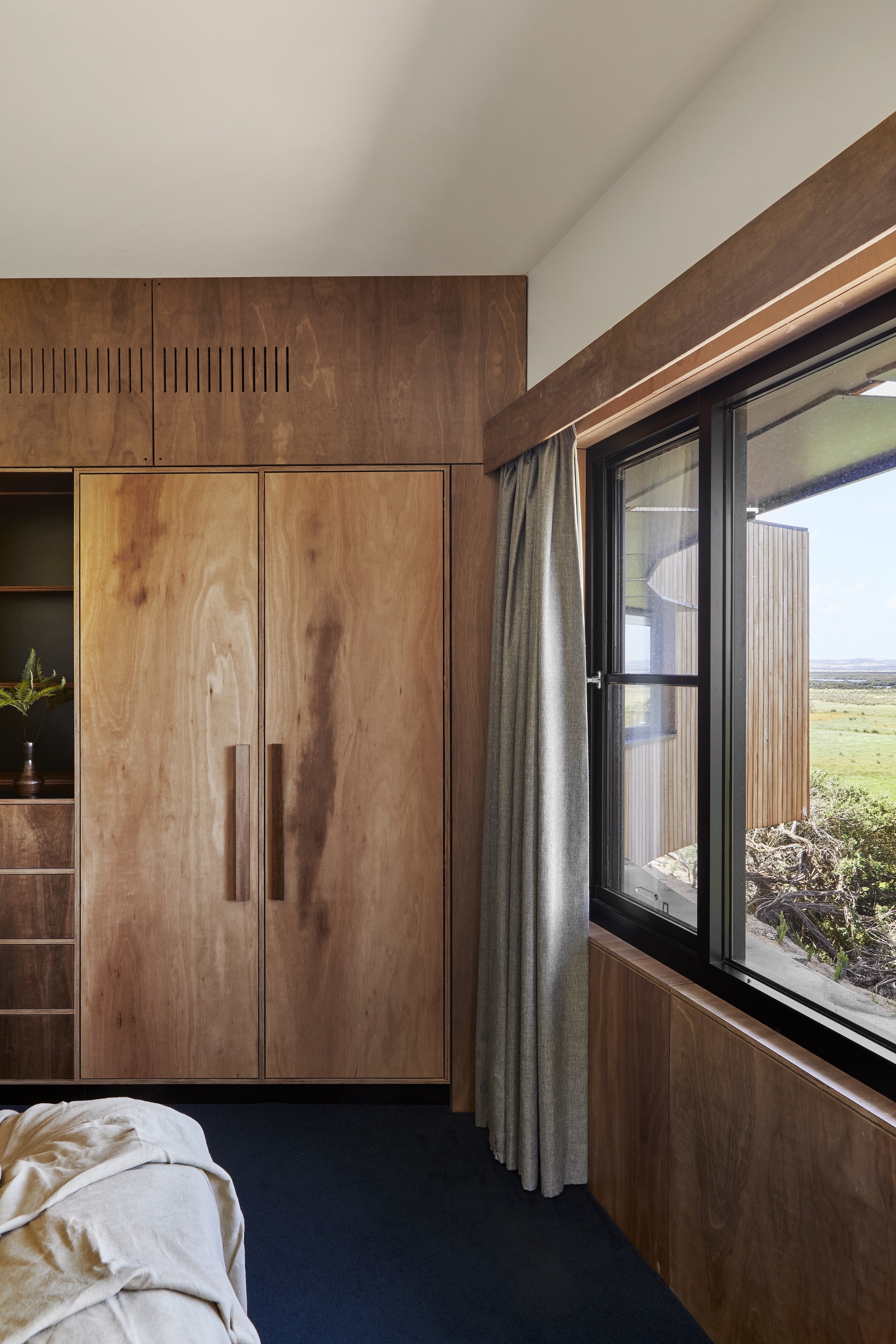 Bedroom with built-in timber cabinetry and corner window overlooking open grassland