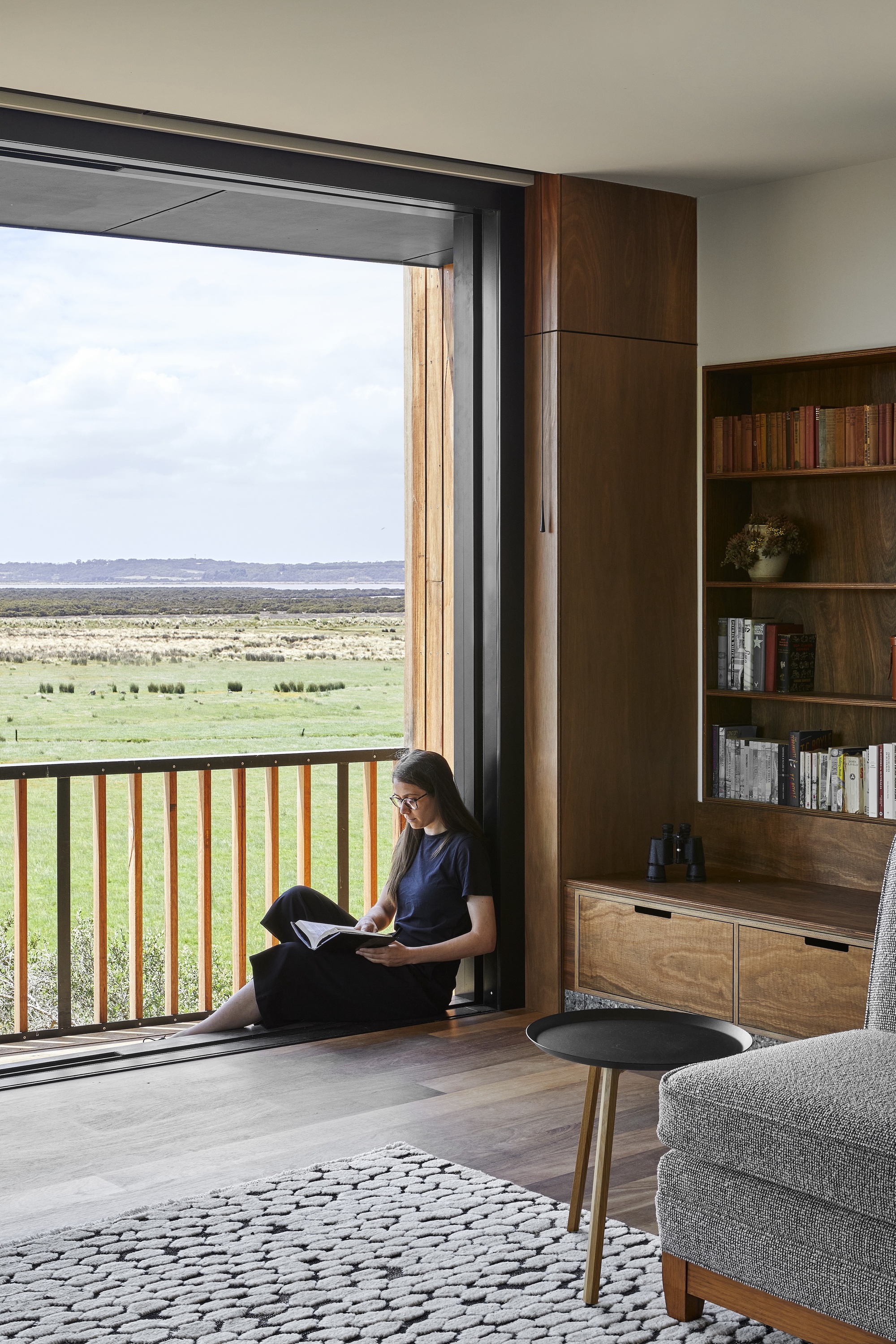 Reading nook beside a sliding door with person seated overlooking expansive green landscape
