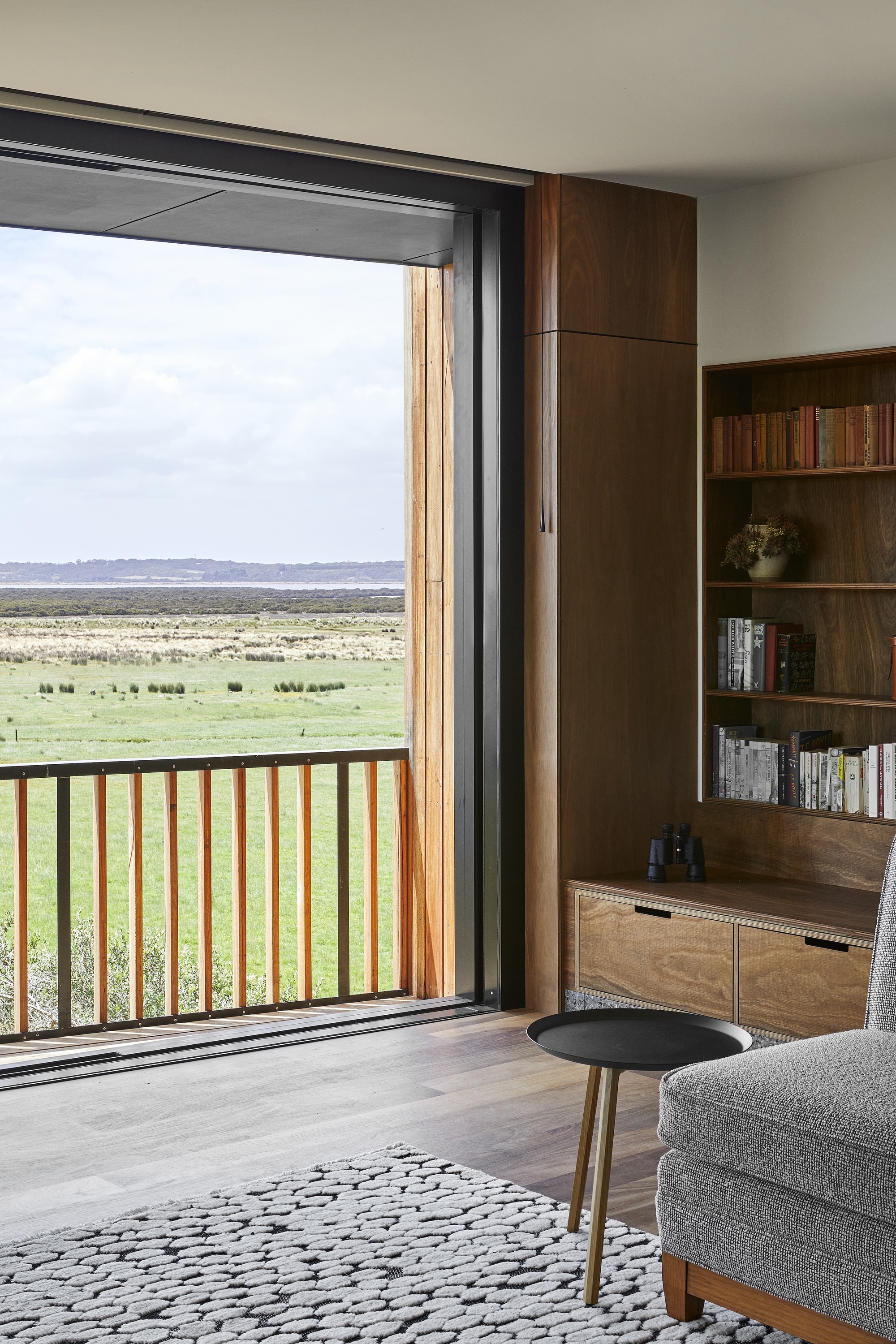 Living room with timber bookshelf beside sliding door opening to a timber-railed balcony