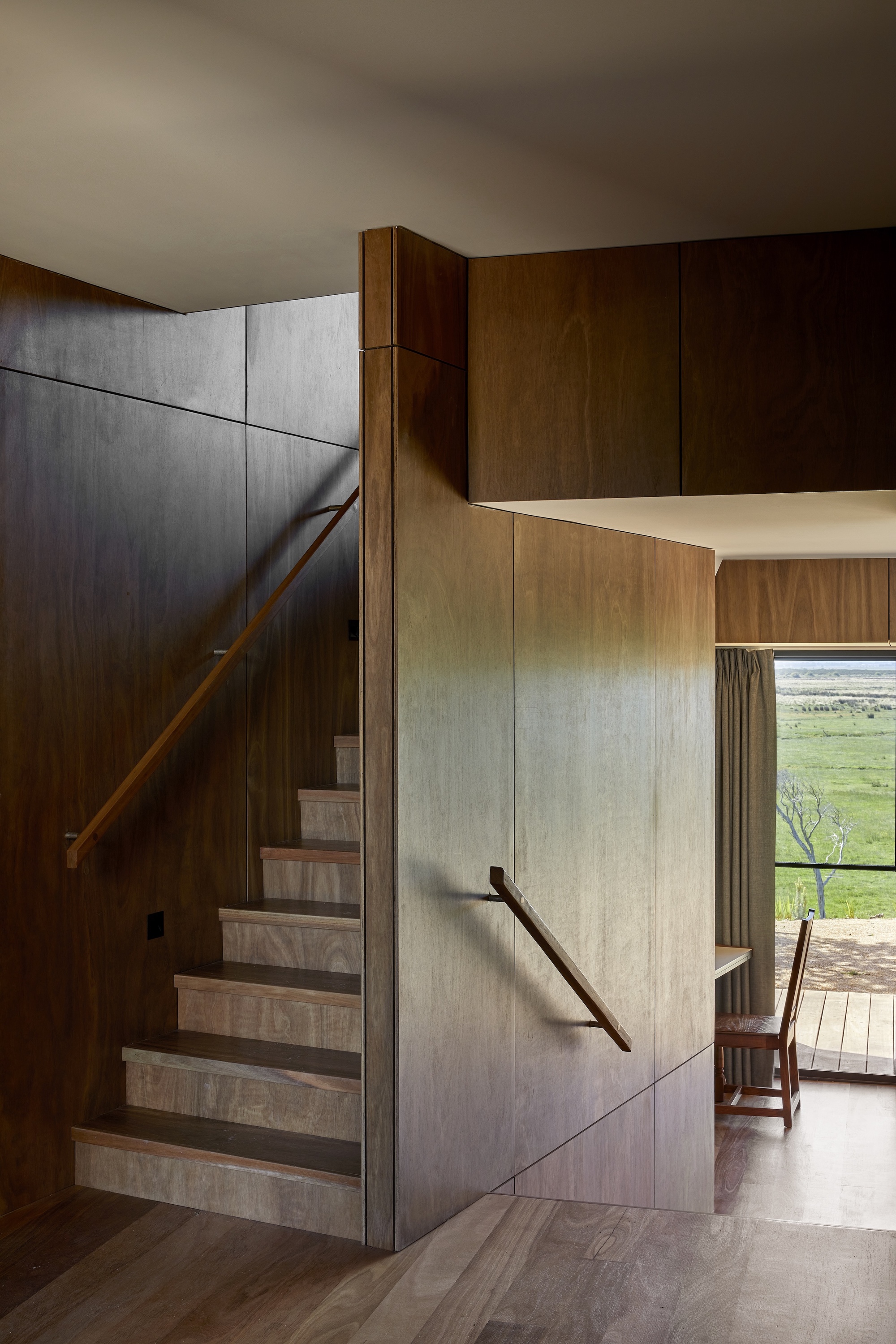 Timber-clad staircase rising between darker and lighter wood paneling with view to green landscape beyond