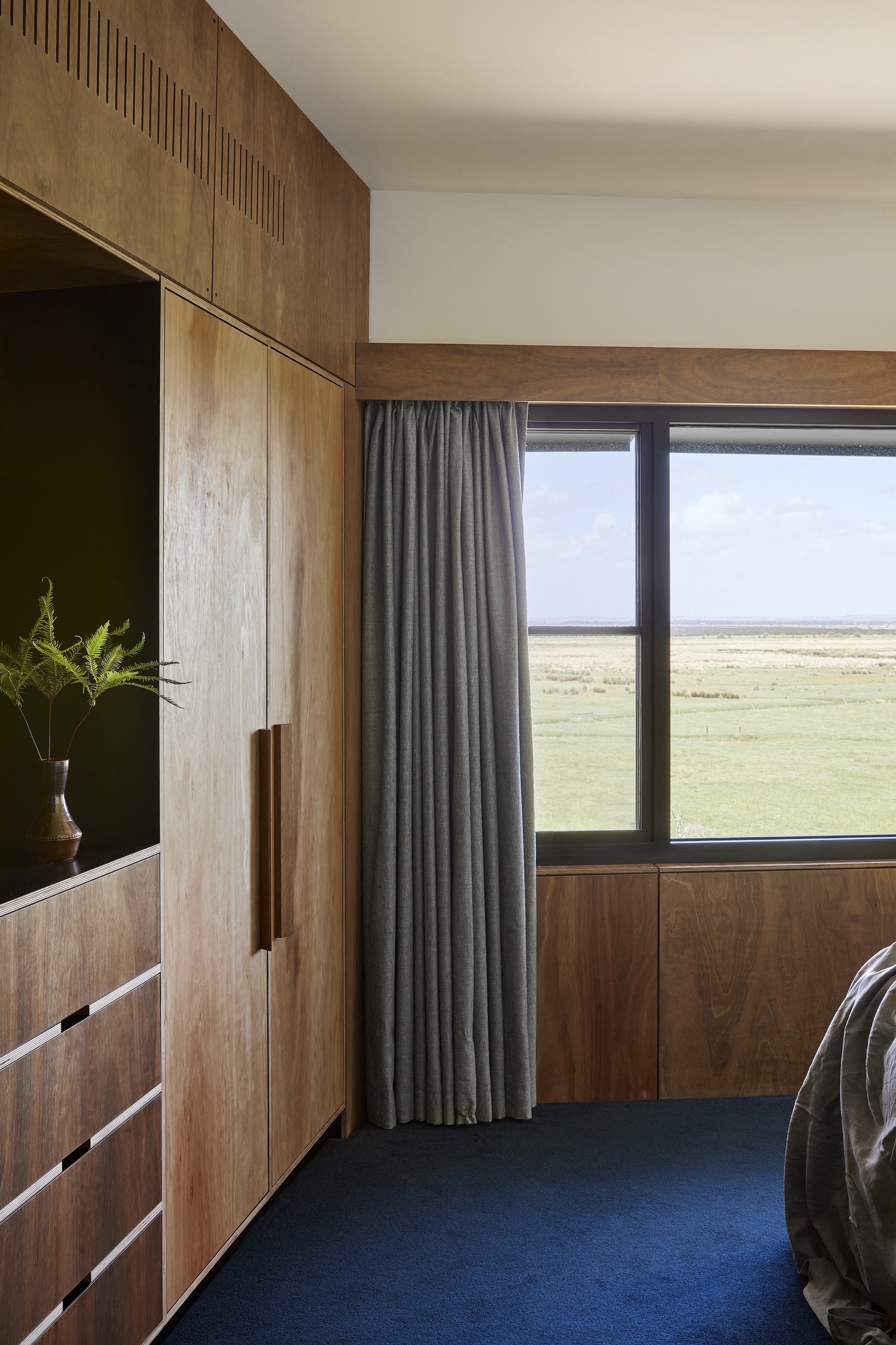 Bedroom with timber built-in cabinetry and grey curtain framing a window overlooking open grassland