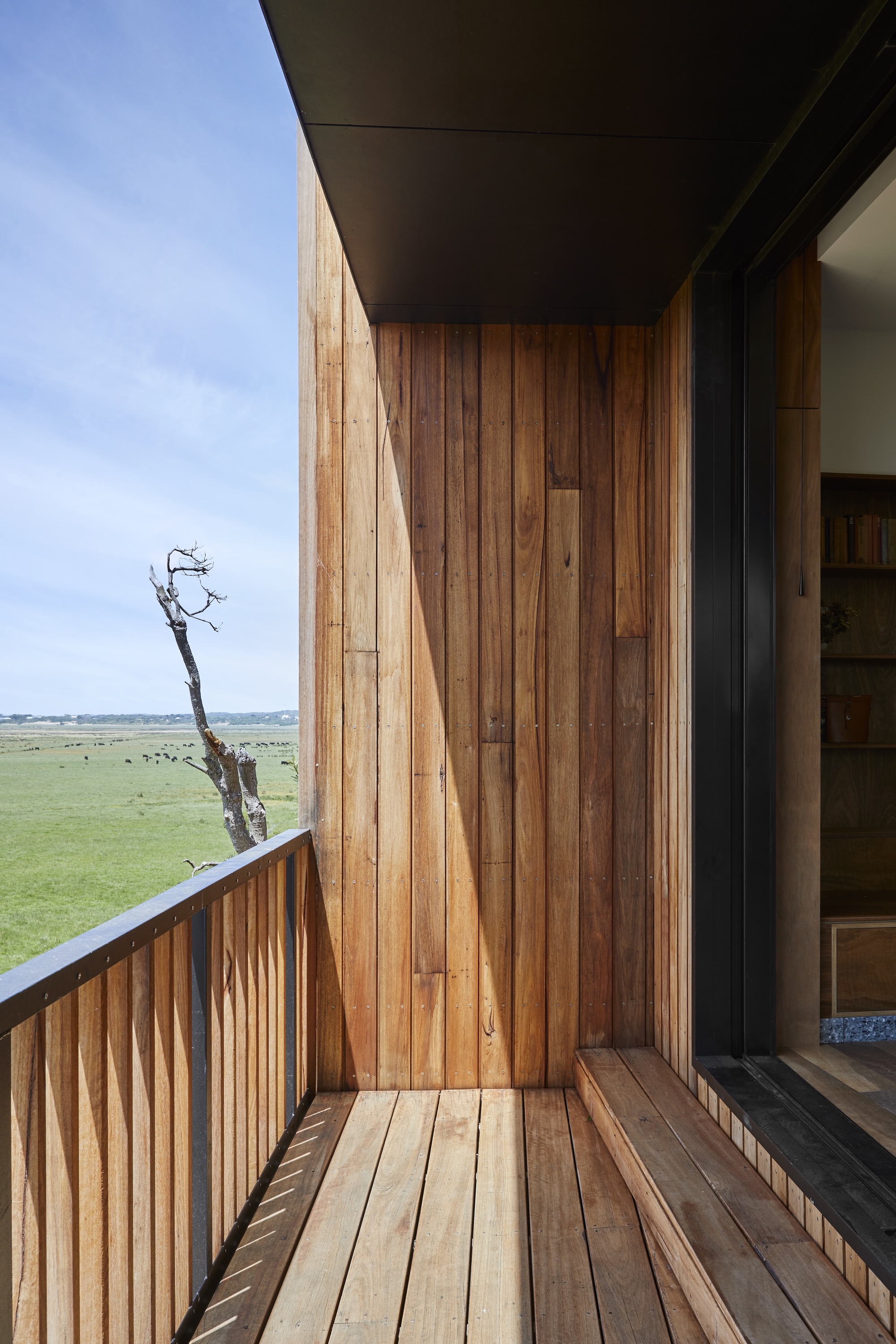 Timber-clad balcony with vertical boarding and decking overlooking a flat green landscape under blue sky