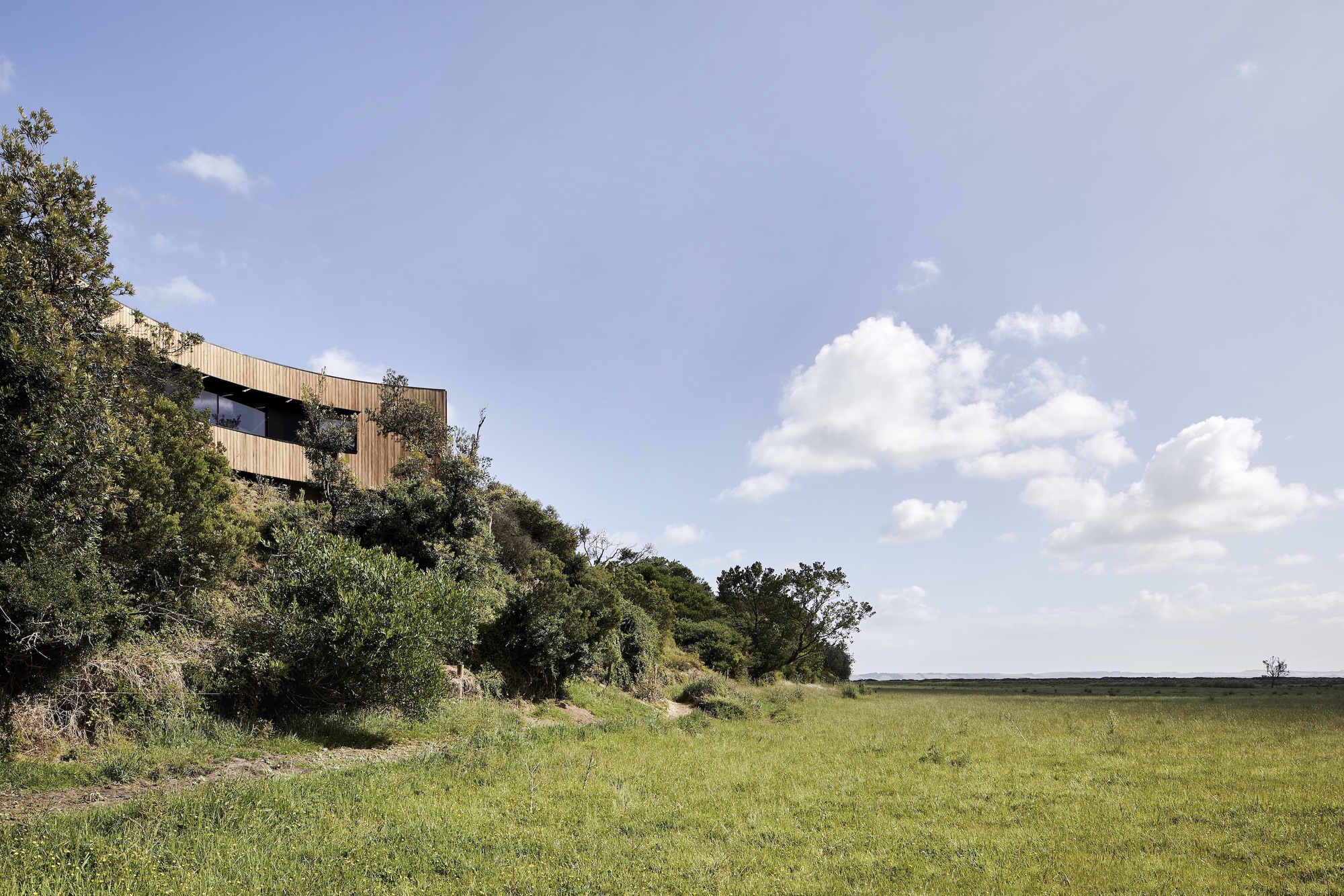 Timber structure nestled into a hillside covered in dense vegetation above an open grassy plain