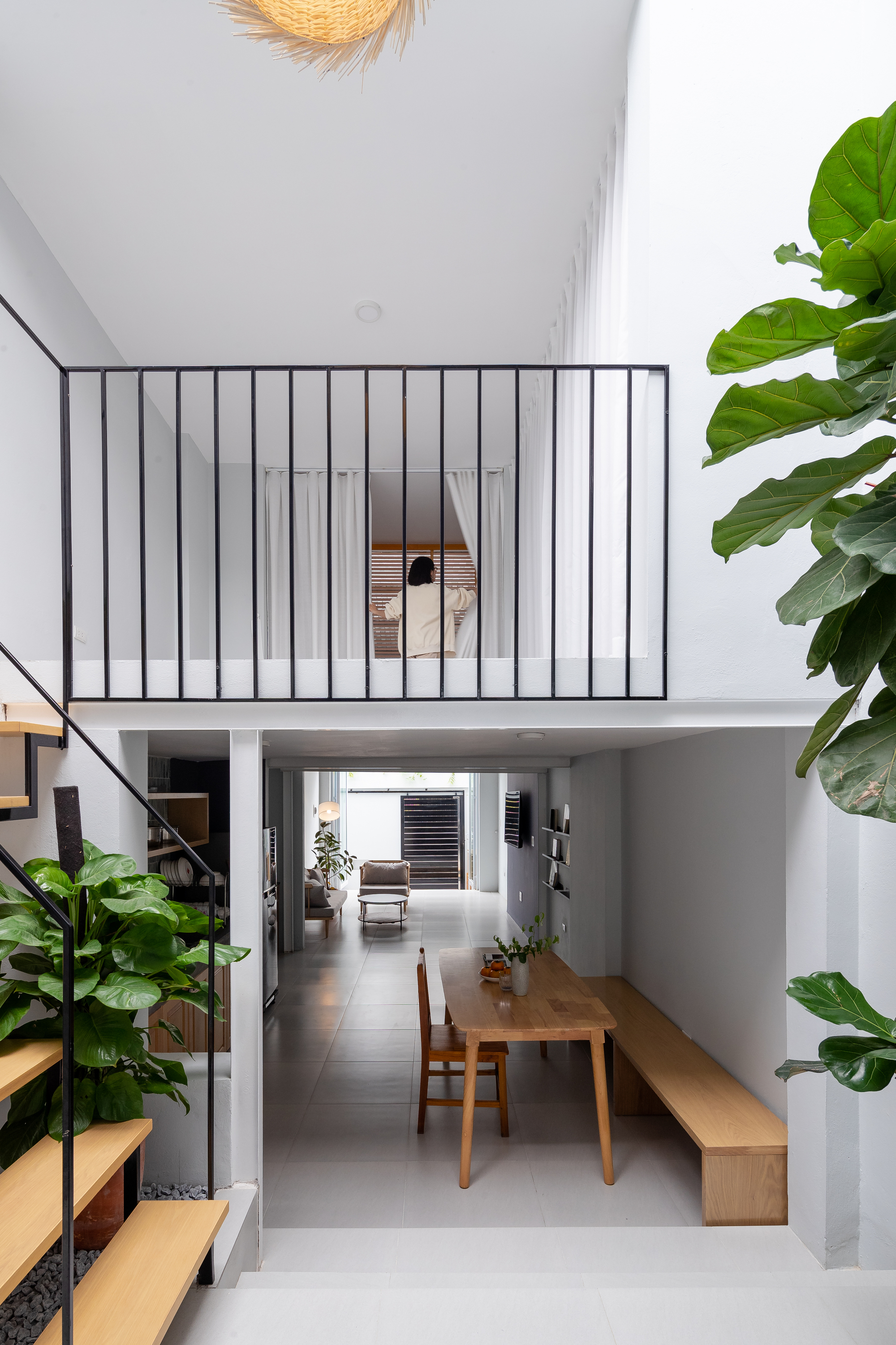 Double-height living space with vertical steel bar mezzanine railing and large potted plants