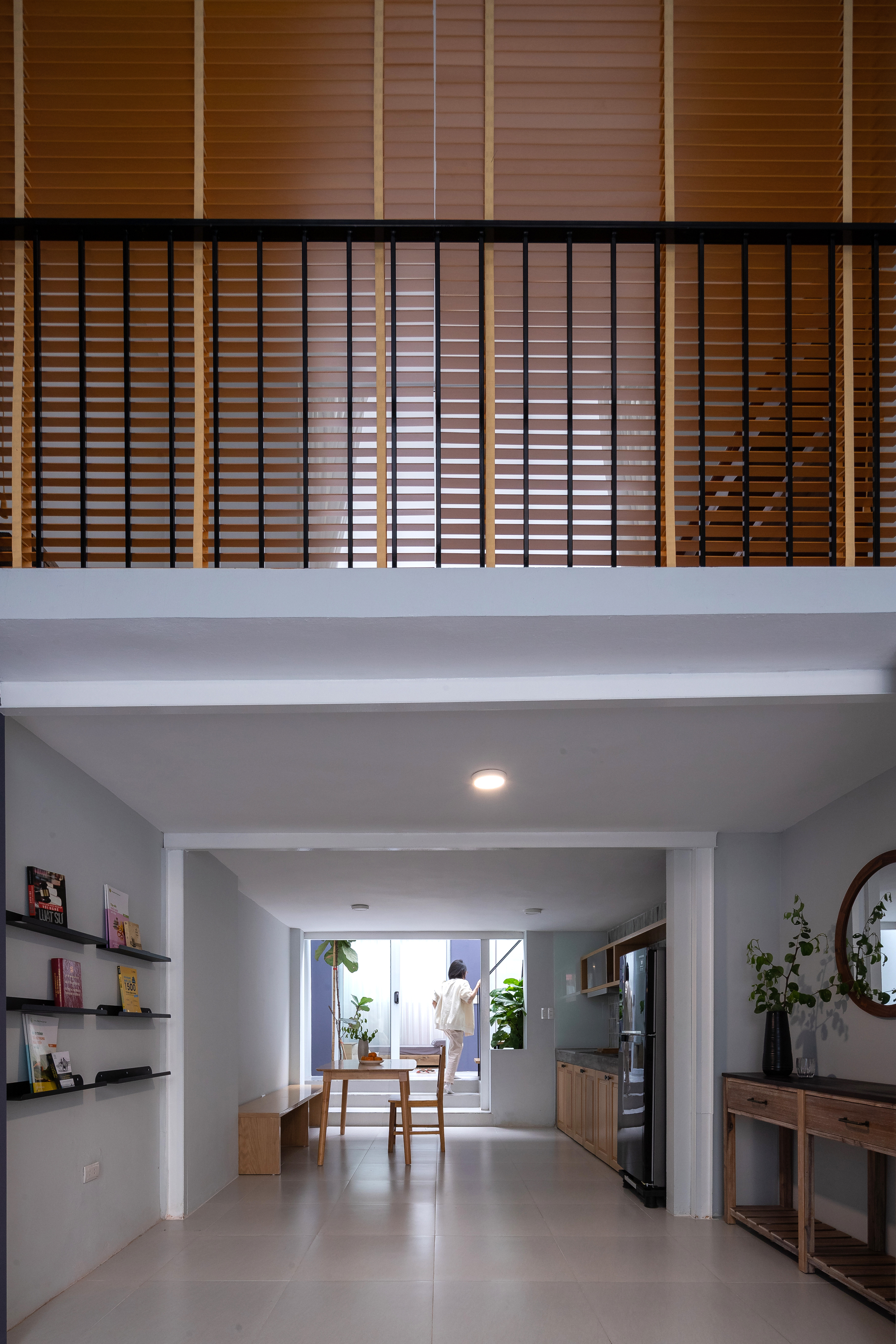 Corridor view beneath mezzanine with horizontal timber slat screen and dining area beyond