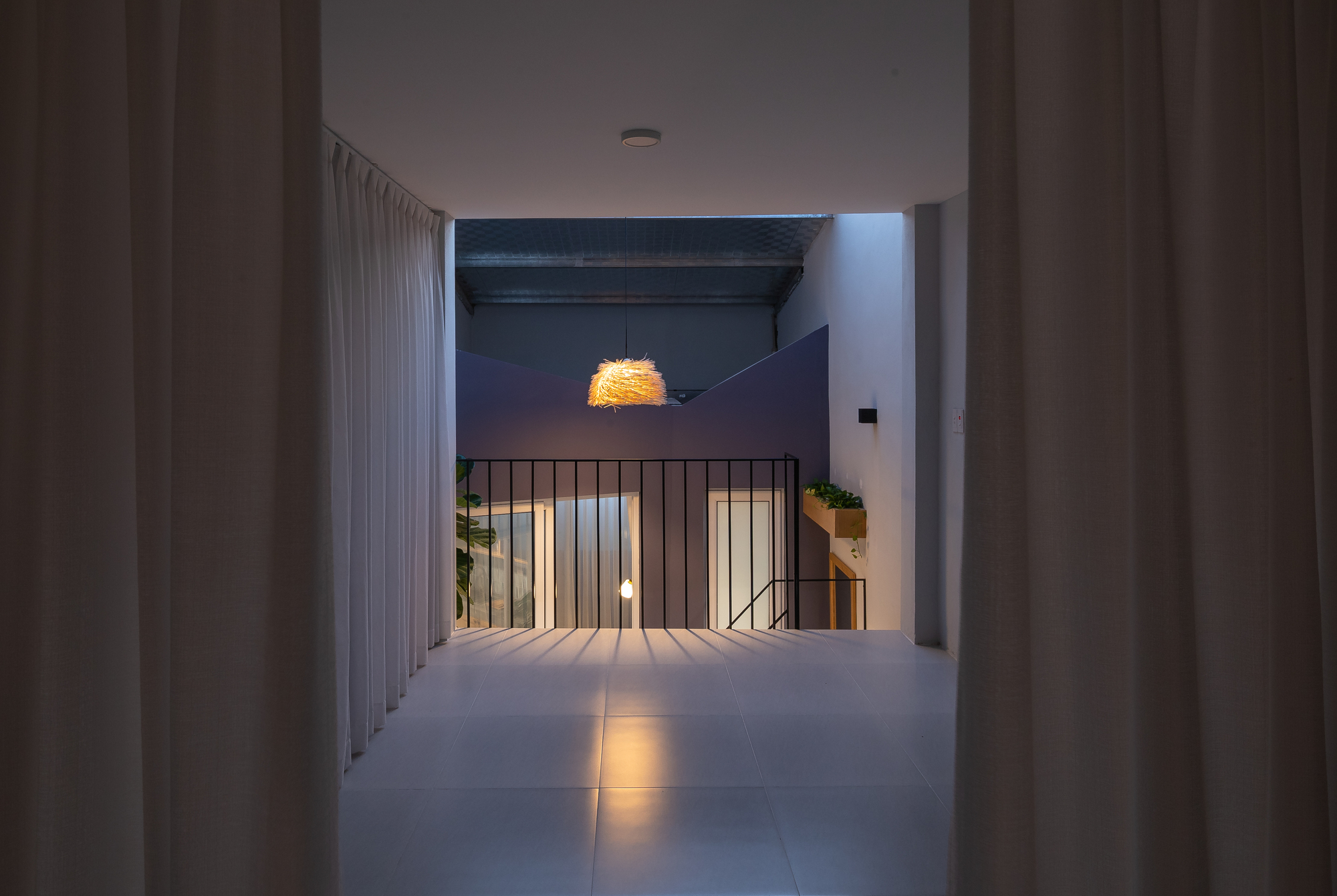 Upper-level corridor at dusk with black steel railing and woven pendant light overhead