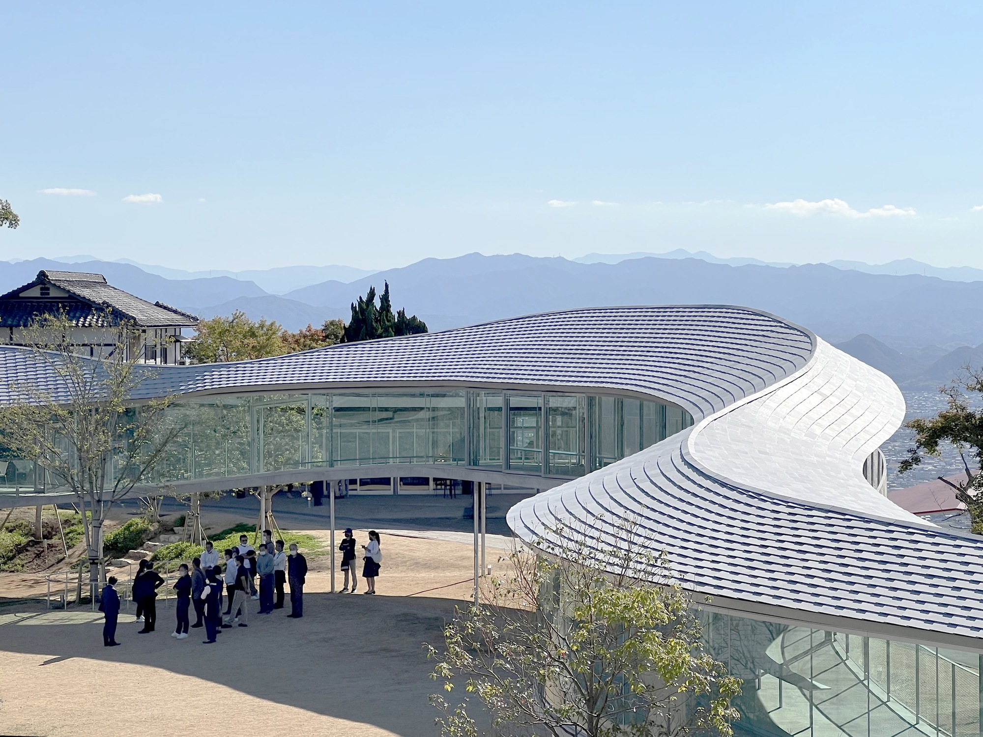Ribbed white roof canopy over continuous glass walls with visitors gathered on the forecourt