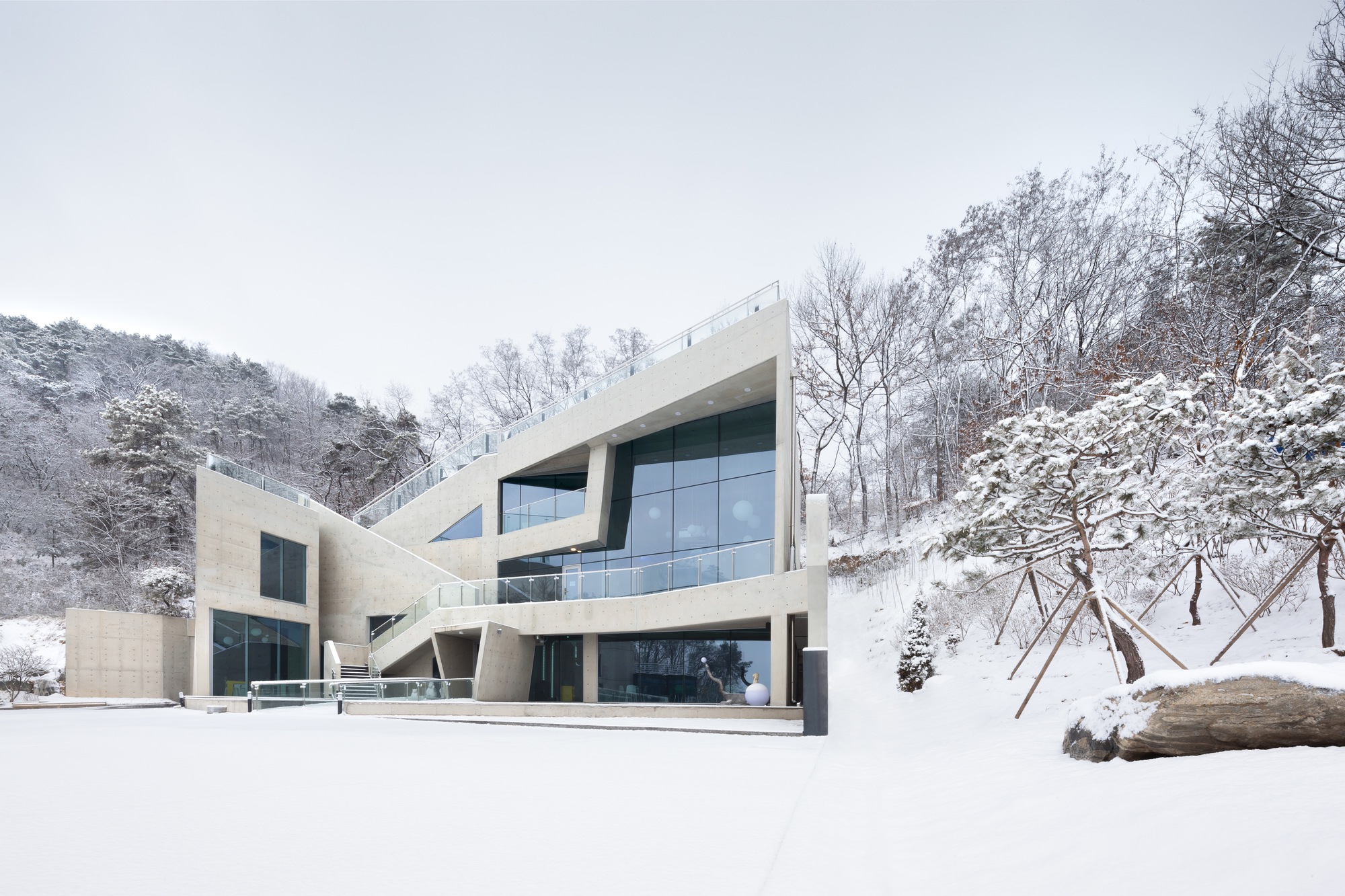 Angular concrete volumes with cantilevered upper floors and full-height glazing set into a snowy hillside