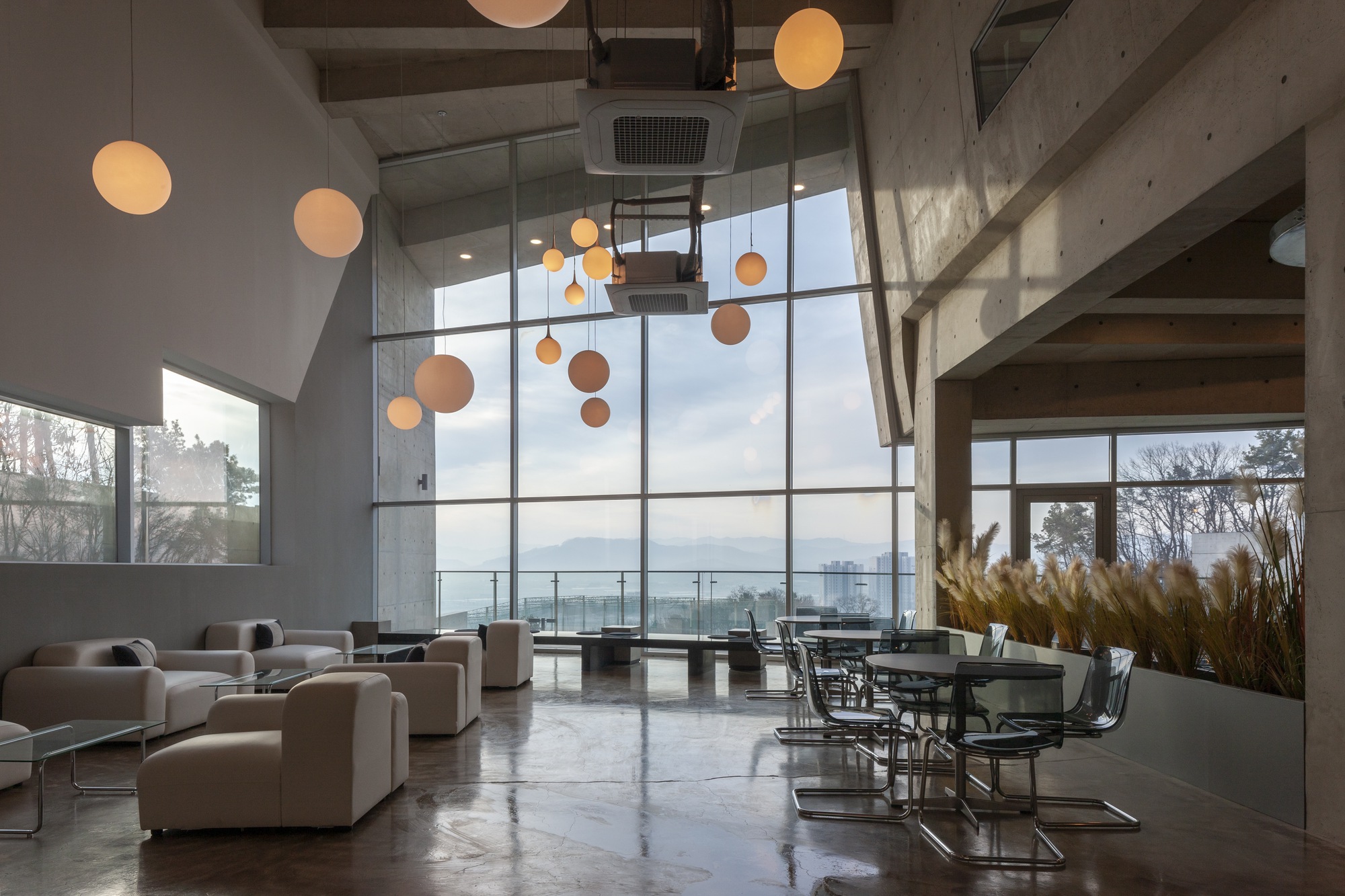 Double-height living space with exposed concrete ceiling, circular pendant lights, and floor-to-ceiling windows overlooking the valley