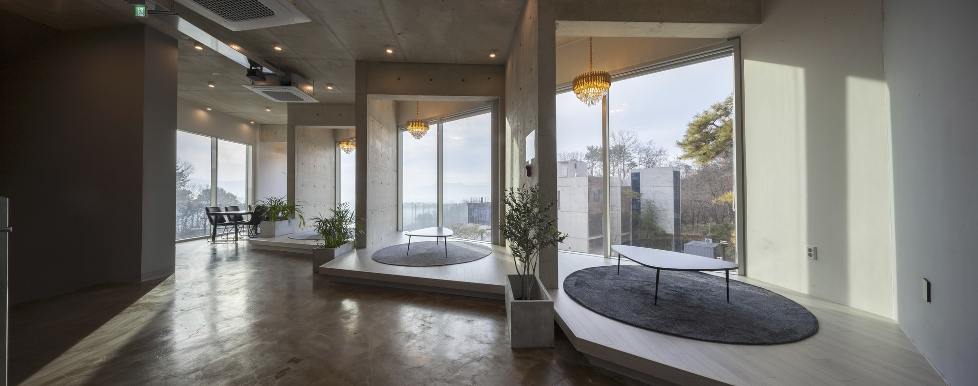 Interior corridor with polished concrete floors, circular recessed seating platforms, and glazed walls opening to the hillside