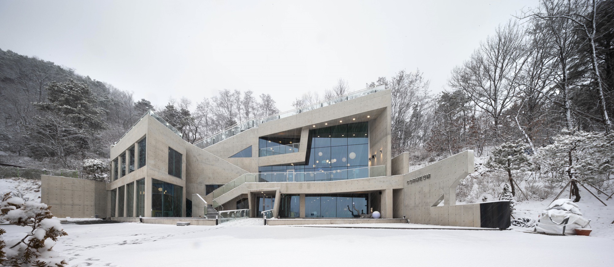 Frontal view of the concrete facade with interlocking volumes and ribbon windows under overcast winter sky