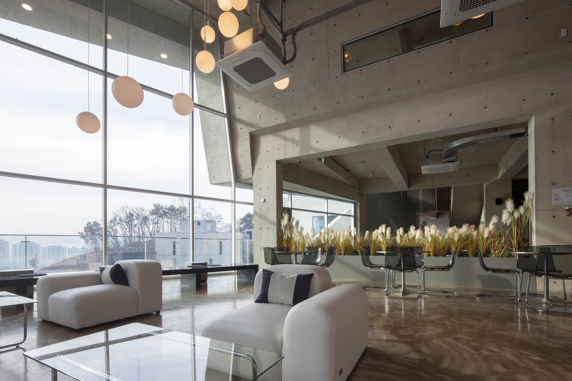 Double-height lobby with concrete ceiling, floor-to-ceiling glazing and pendant lighting above seating