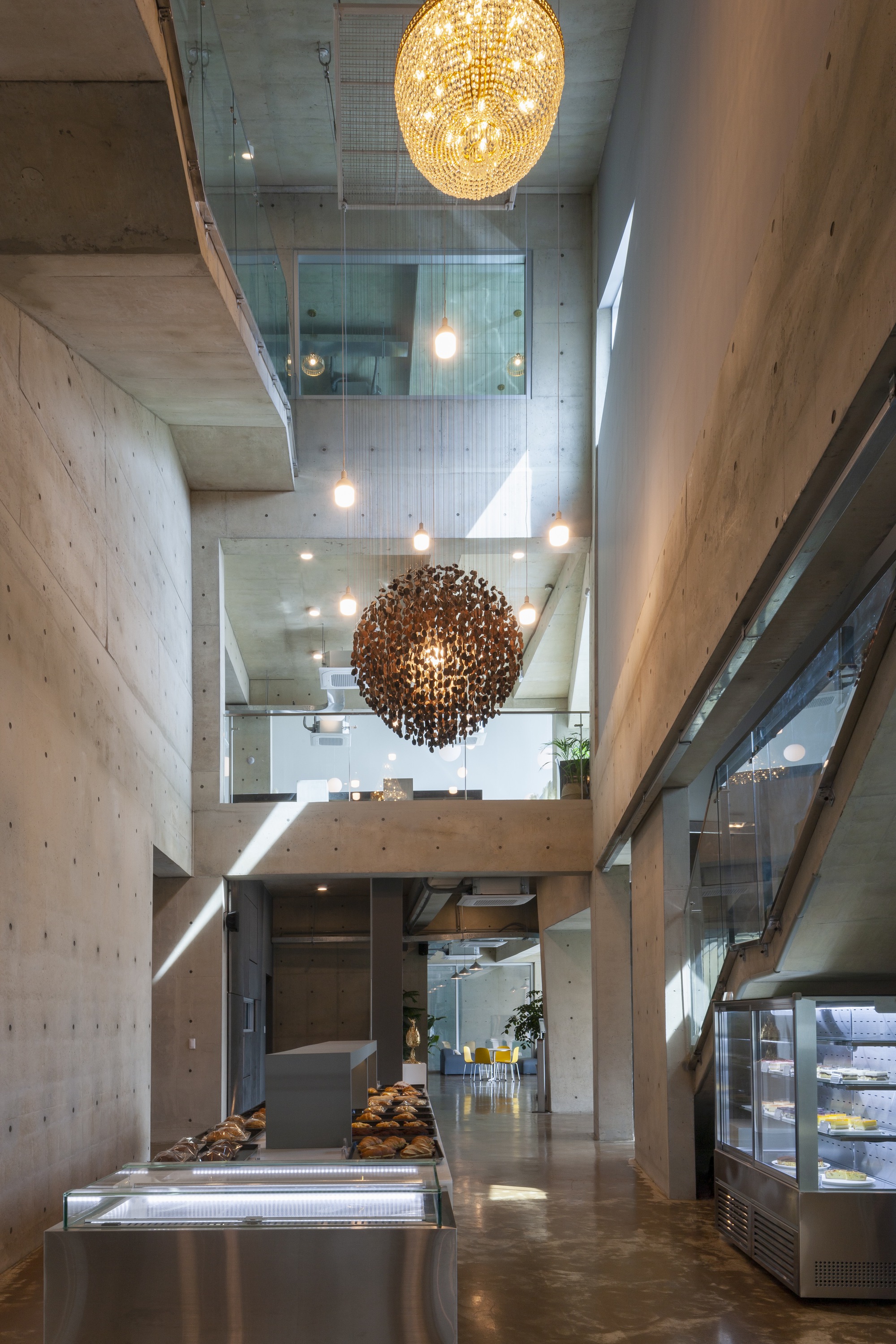 Vertical view through atrium showing stacked concrete floors, glass railings and spherical pendant fixtures