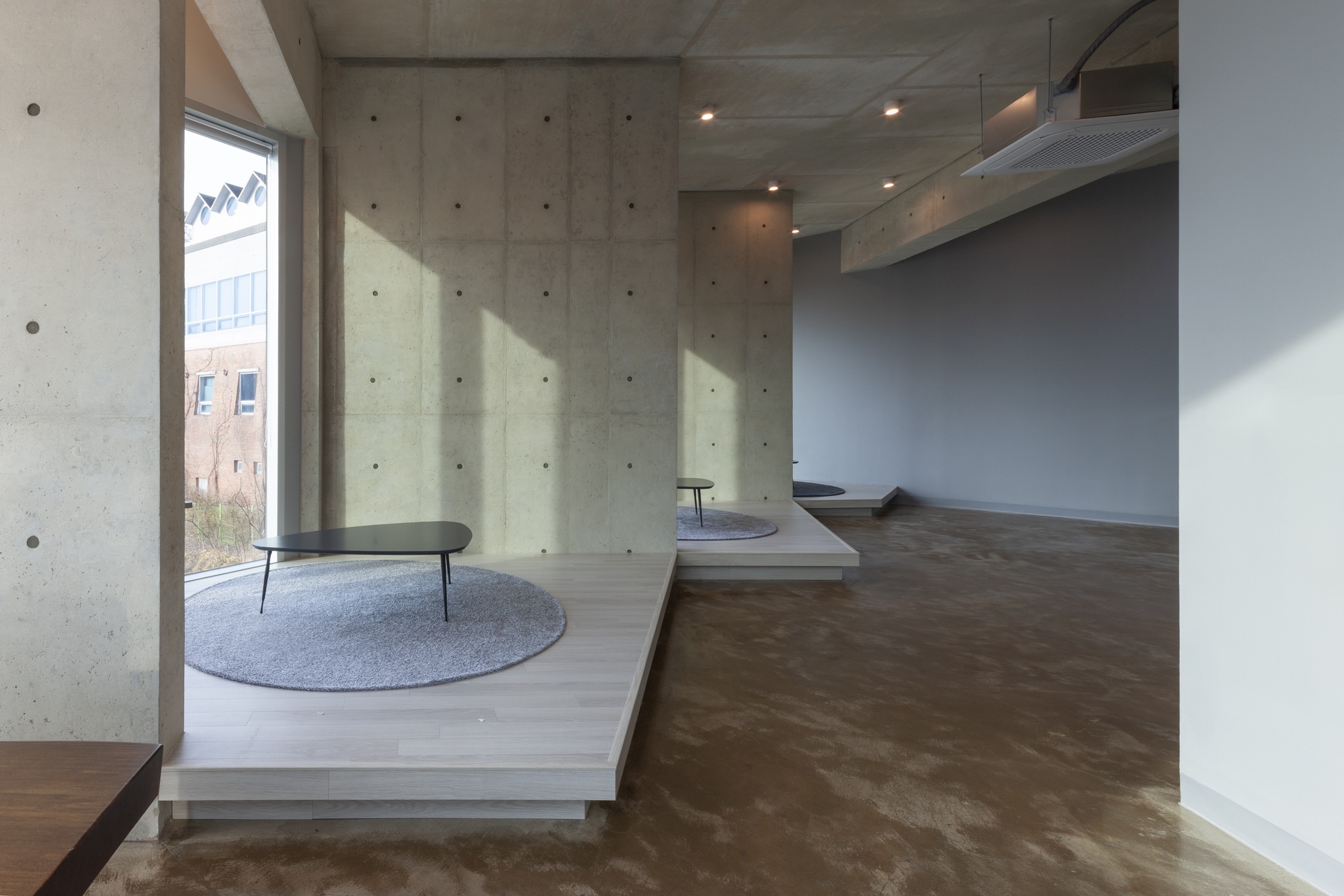 Polished concrete floors meeting raised timber platforms beneath board-formed concrete walls