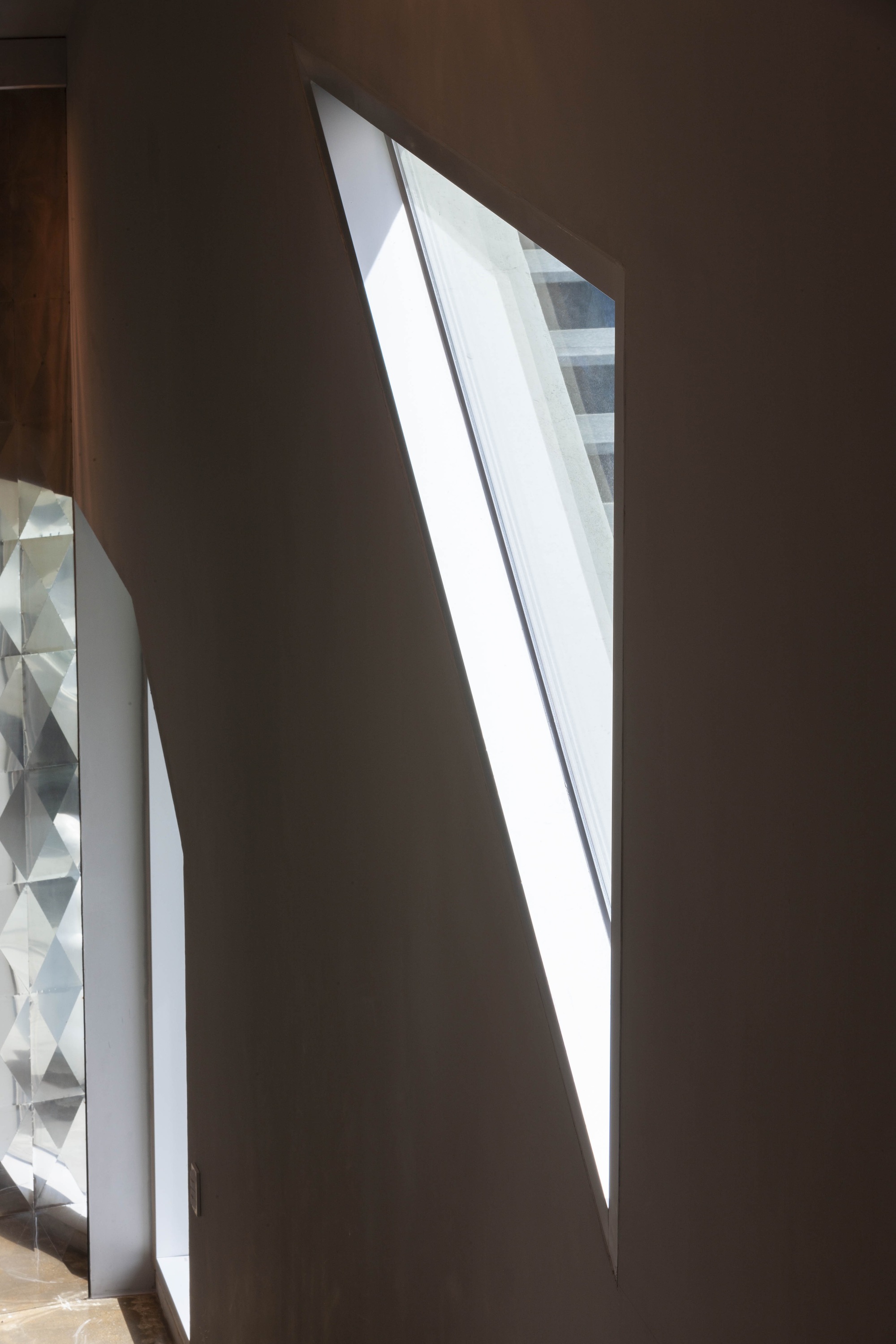 Angled skylight slicing through a dark interior wall with daylight spilling onto the floor