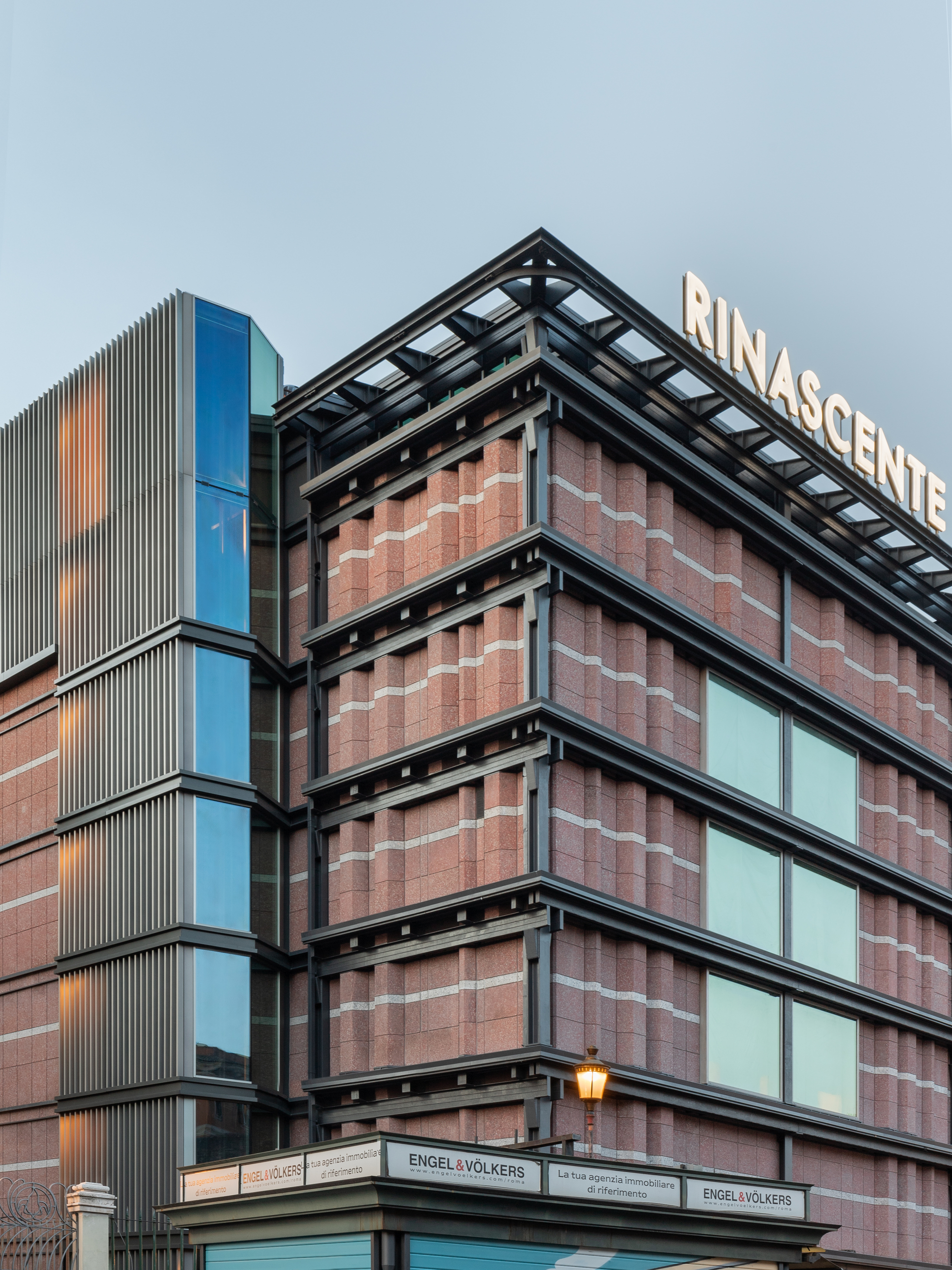 Corner junction of terracotta paneled facade with exposed steel frame and adjacent corrugated metal facade at dusk