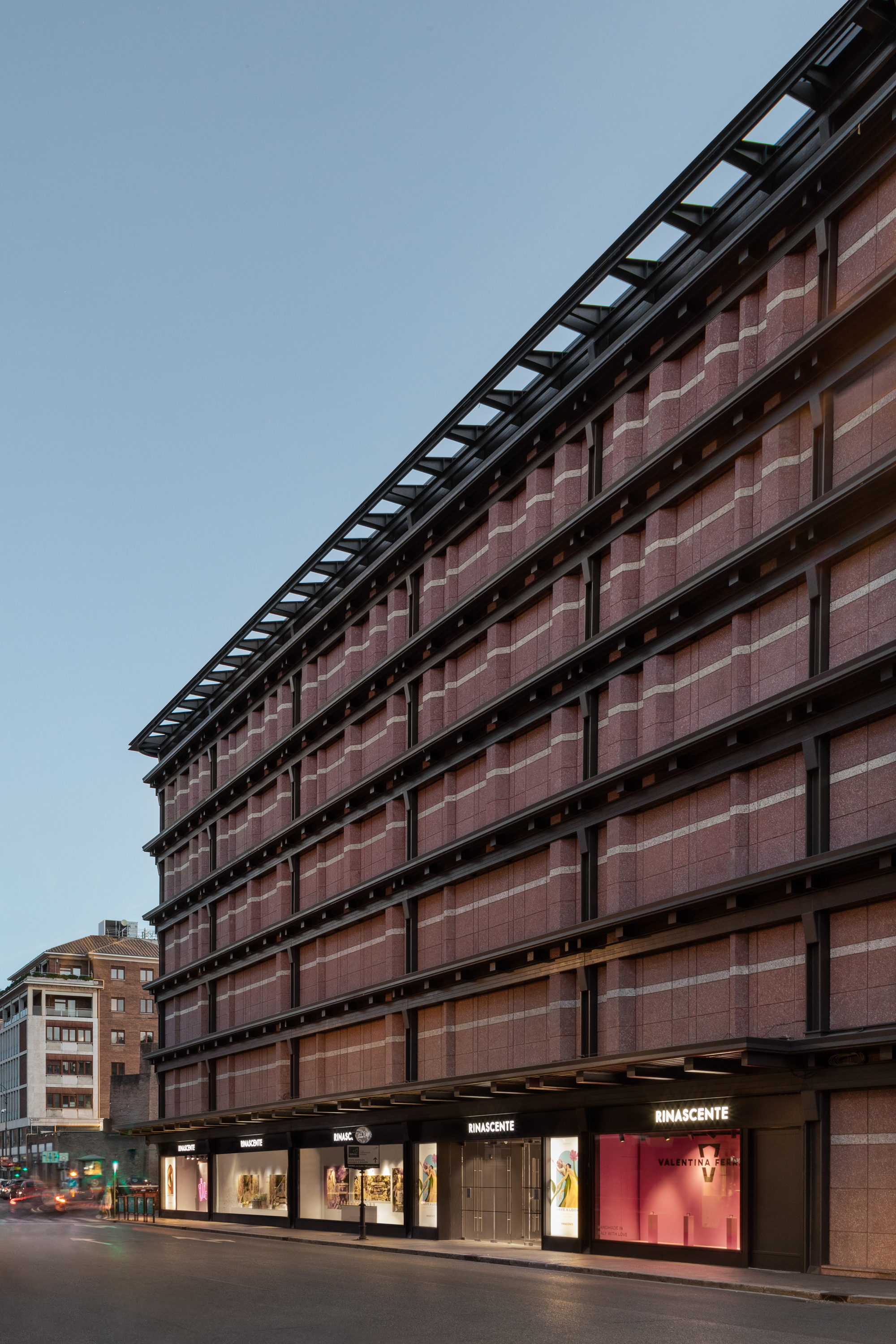 Street elevation with terracotta tile curtain wall and black structural frame at dusk