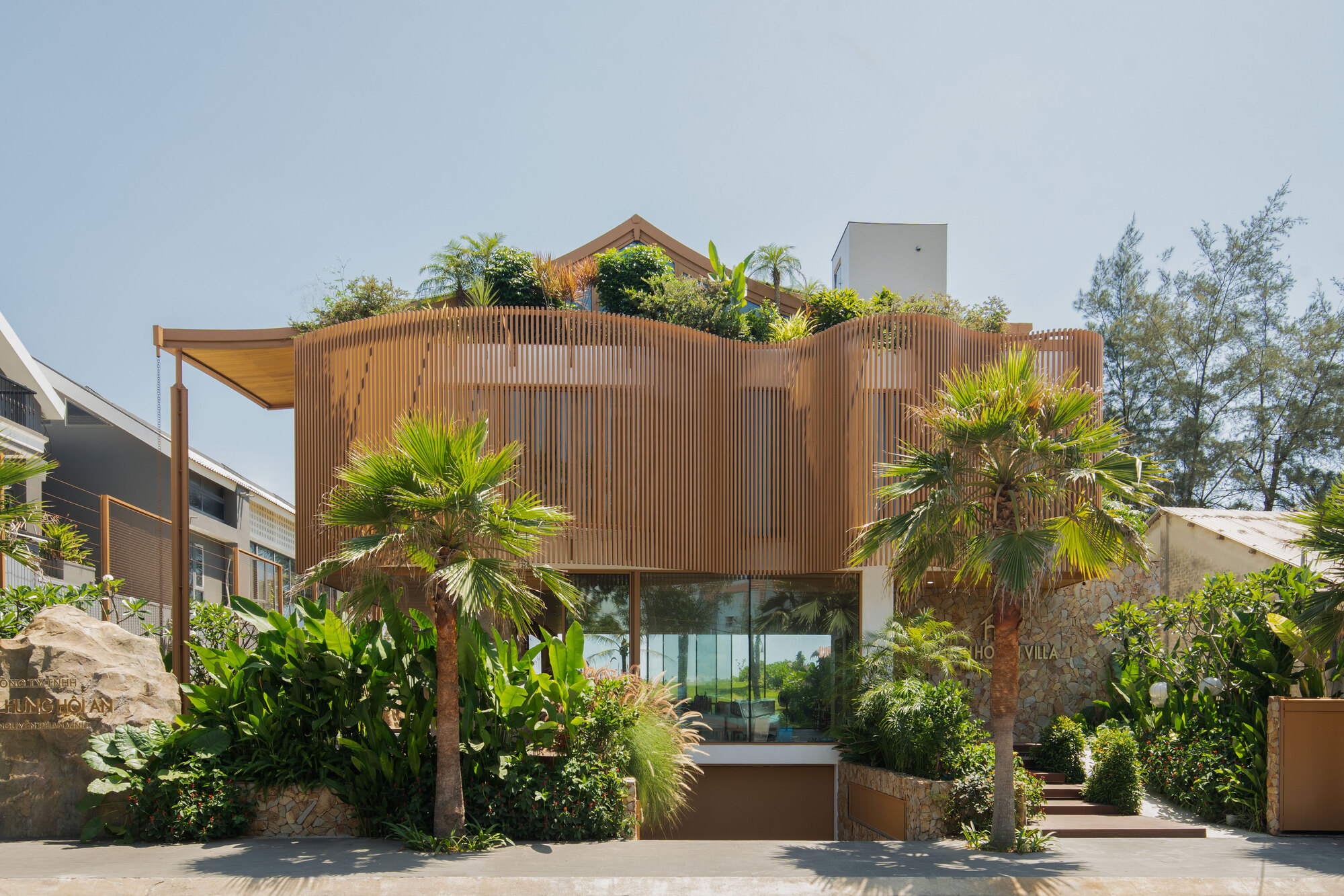 Vertical timber screen facade with rooftop planting and palms framing the entry below