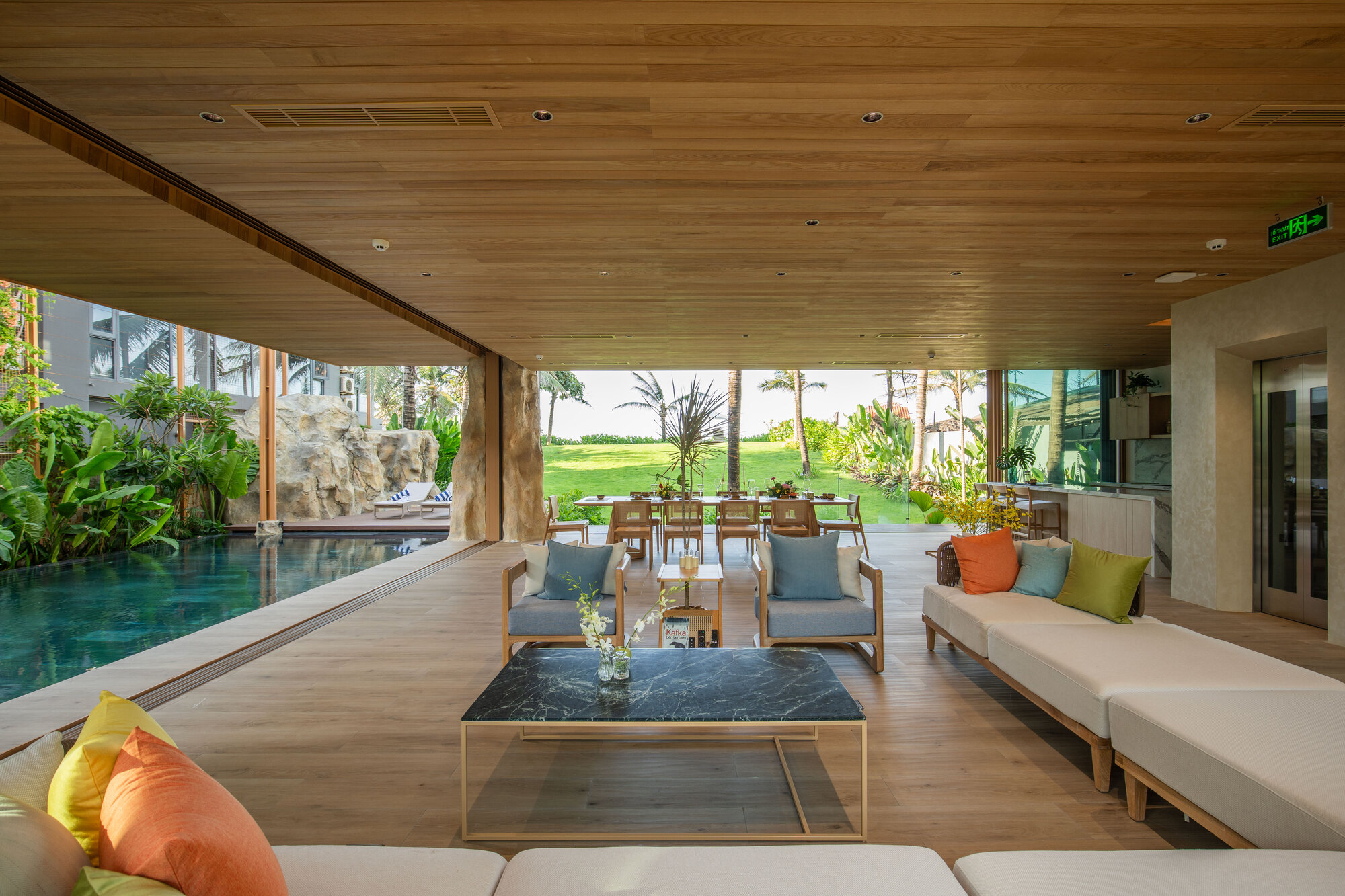 Open living pavilion with timber ceiling looking through to dining area and lawn beyond reflecting pool