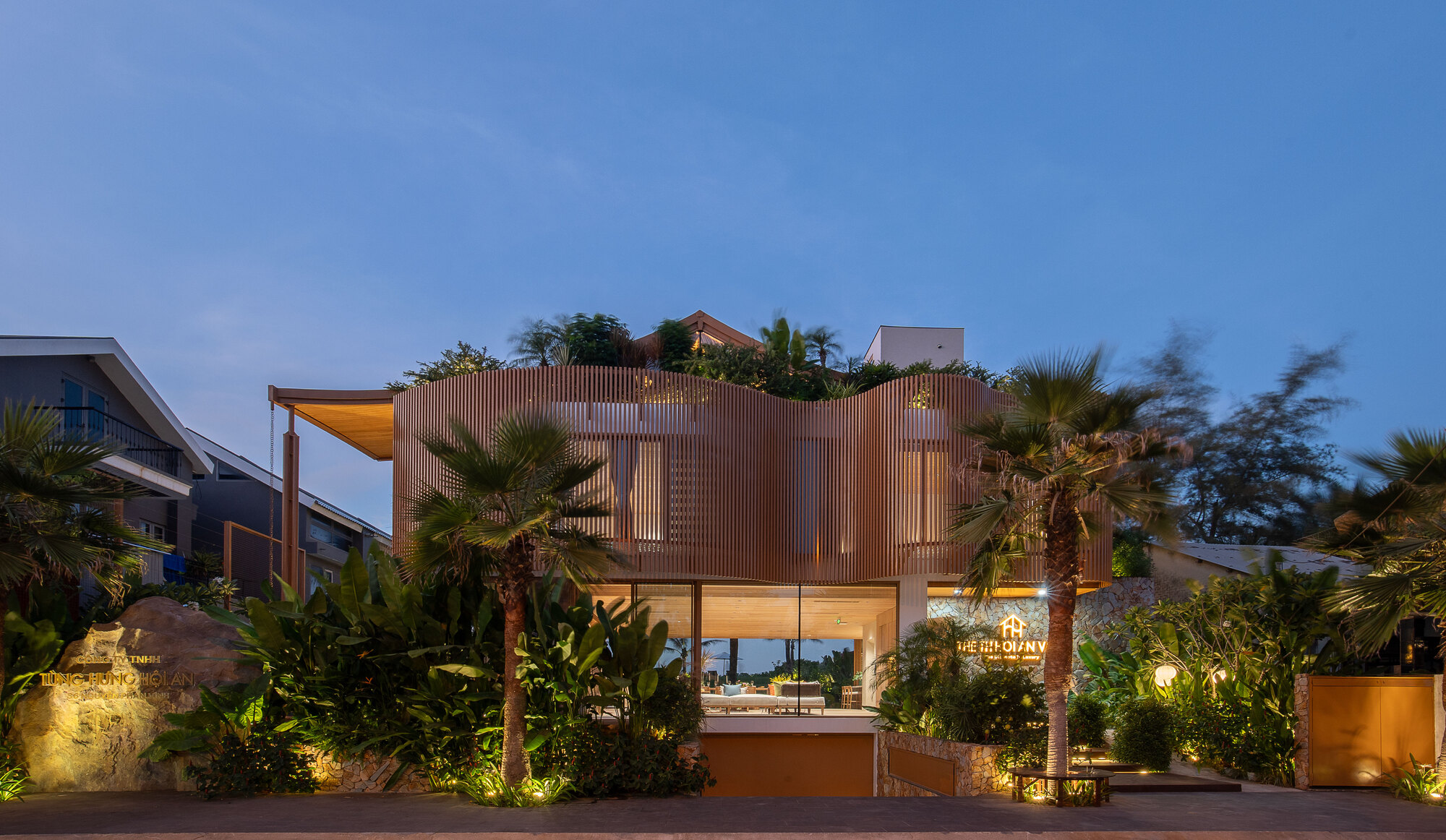Front elevation with vertical timber screens and planted landscape illuminated at twilight