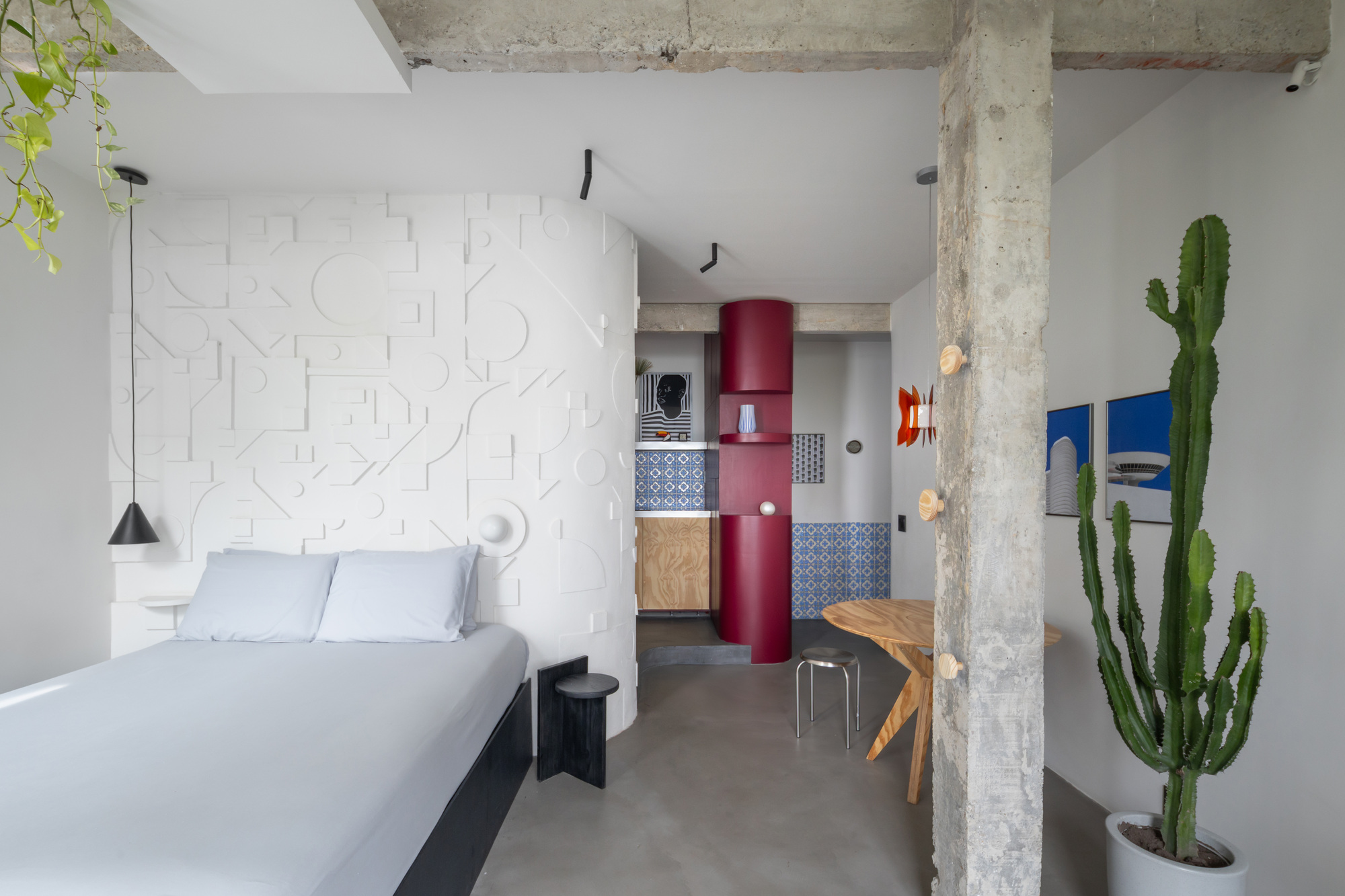 Studio space with exposed concrete ceiling, white relief wall panel, and tall cacti beside a weathered column