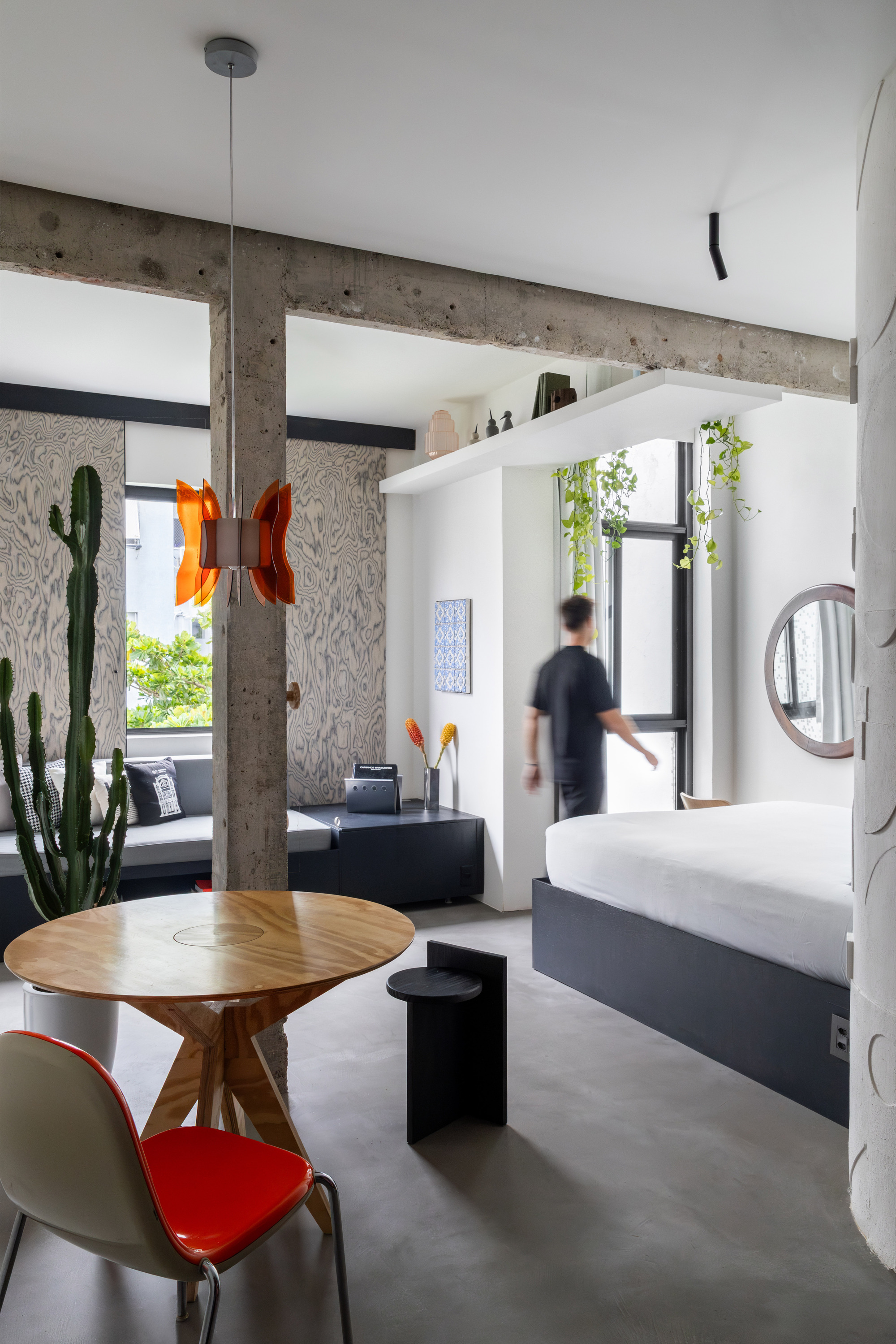 Open living area with exposed concrete beam, white volume, and a figure in motion near the window