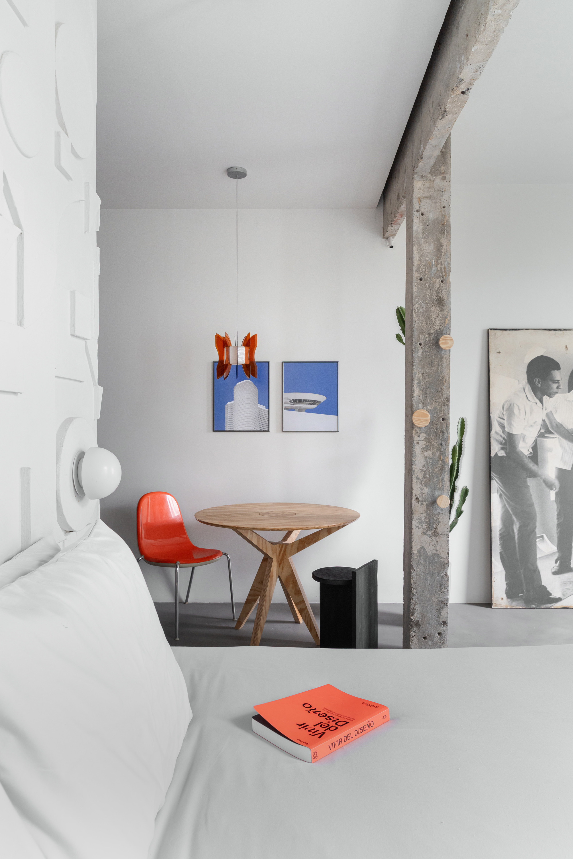 Sitting nook with round timber table, red chair, and artwork against a white wall beside concrete column