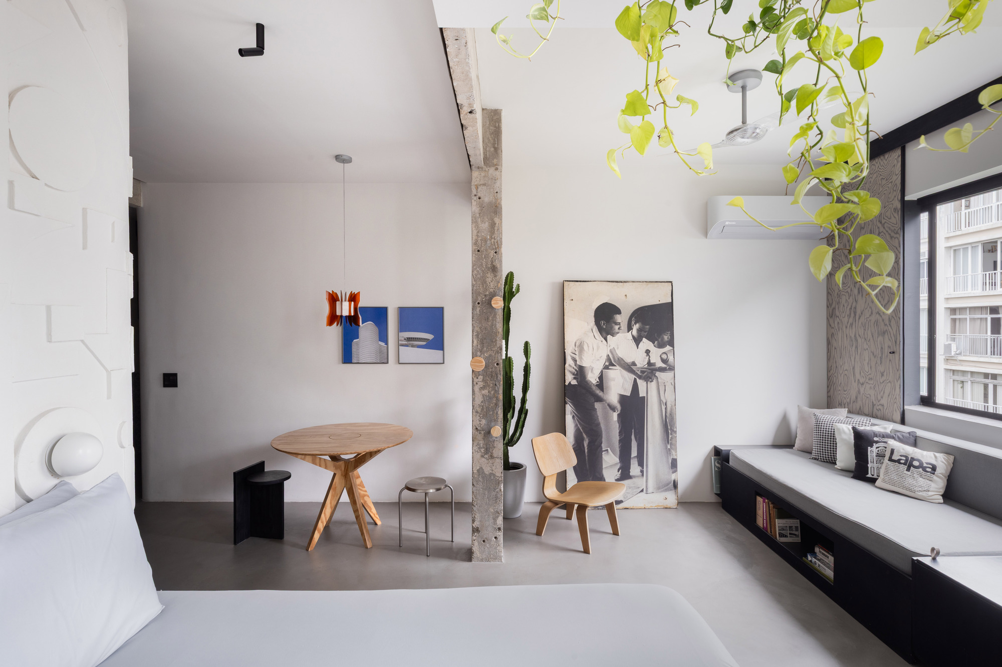 Living space with exposed concrete column, hanging plants, polished concrete floor, and low window seat with storage