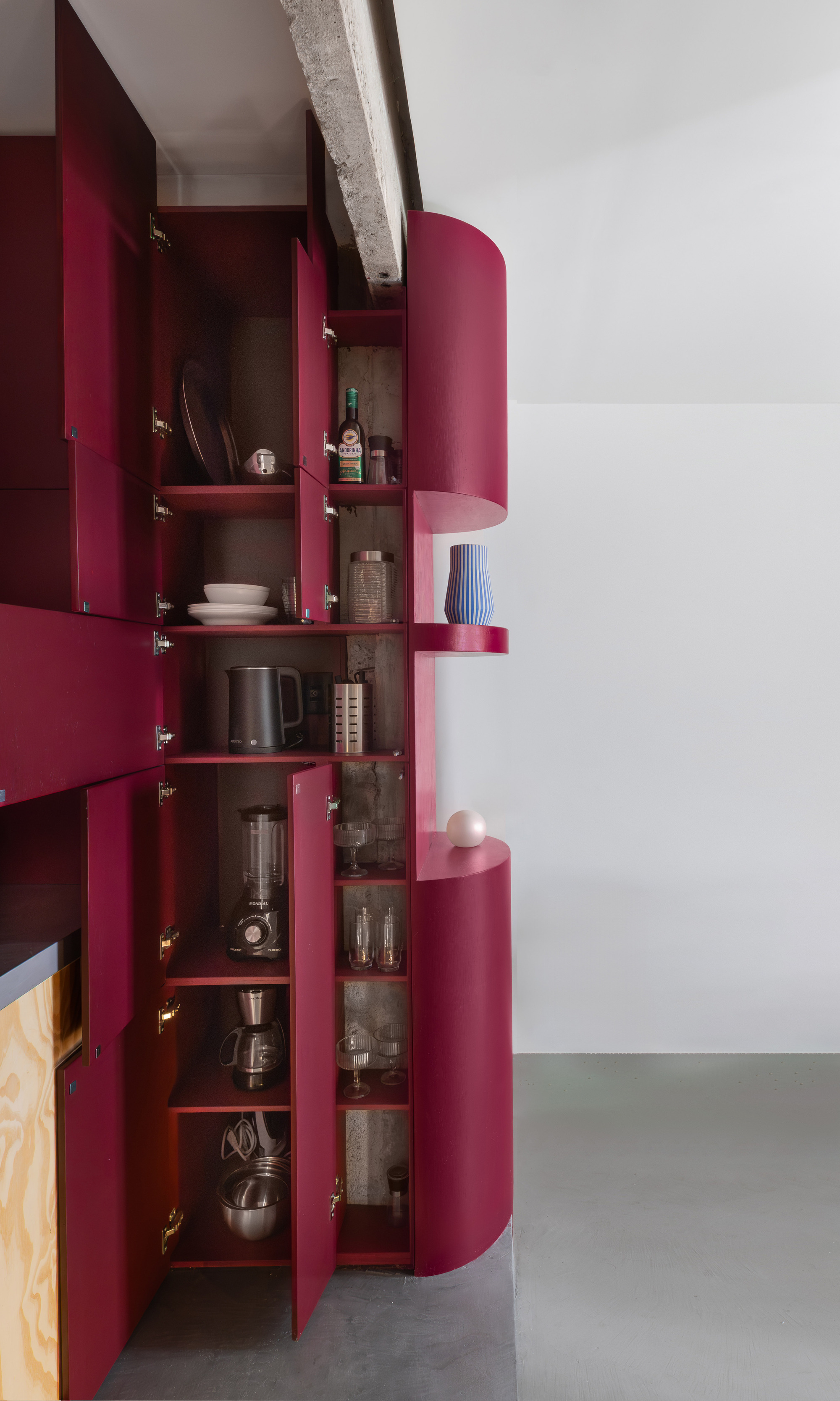 Open burgundy storage cabinet revealing shelves with kitchen appliances and glassware inside the cylindrical volume