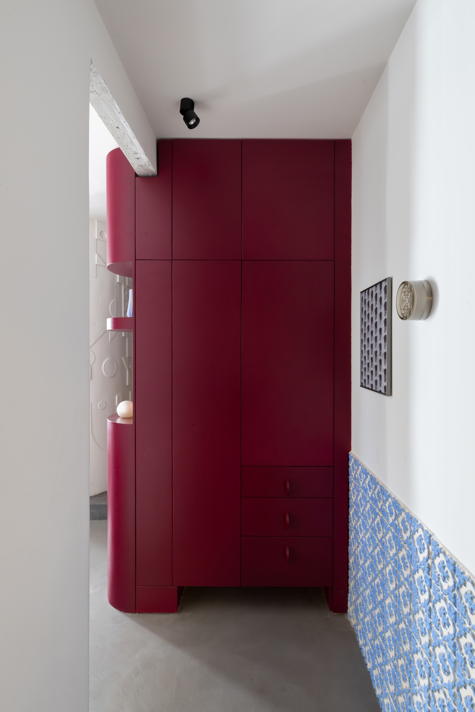 Floor-to-ceiling burgundy storage unit in a hallway with blue patterned tile baseboard and white walls