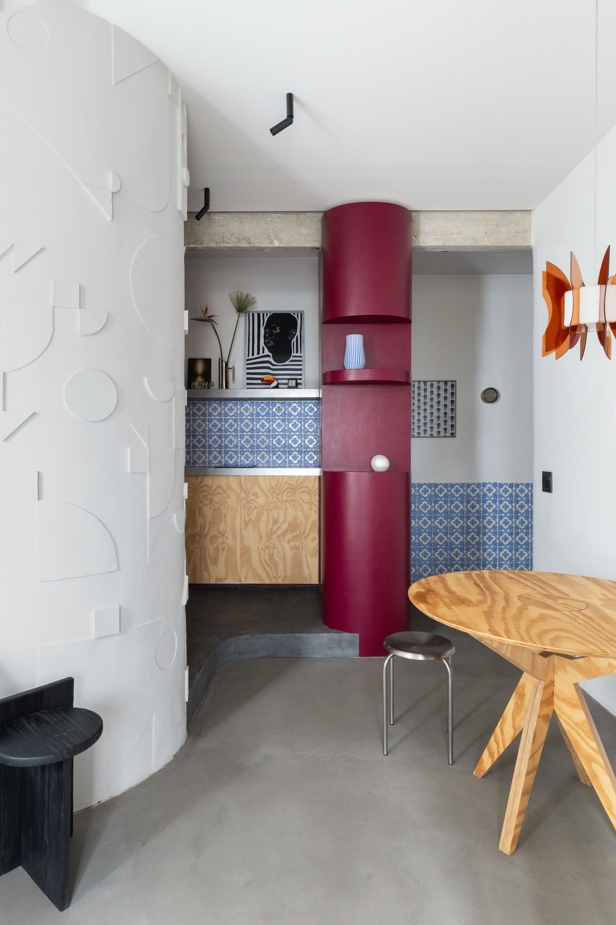 Kitchenette with blue patterned tile backsplash, plywood cabinetry, and a freestanding burgundy cylindrical element