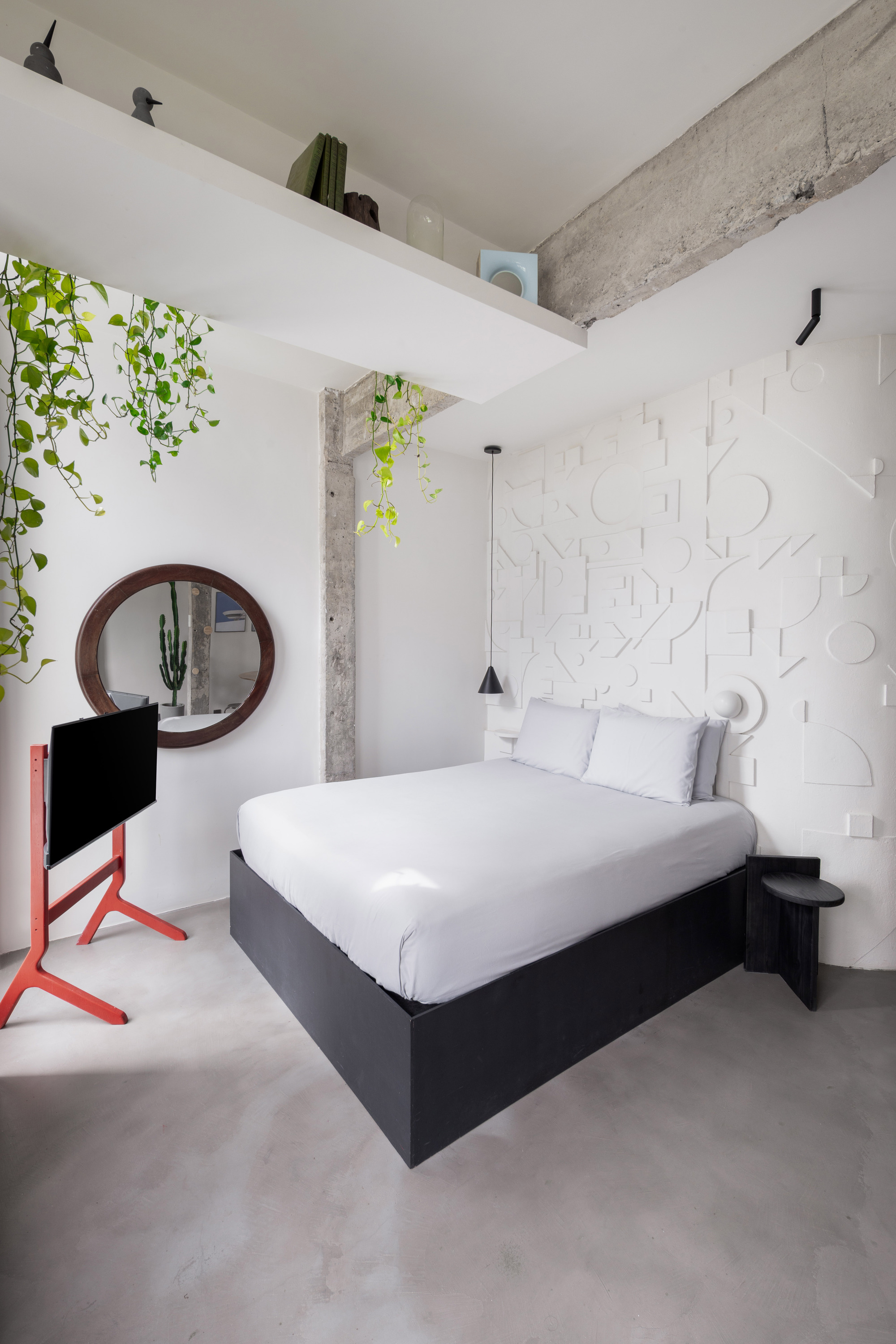 Bedroom with white relief wall panels and trailing plants above exposed concrete beams