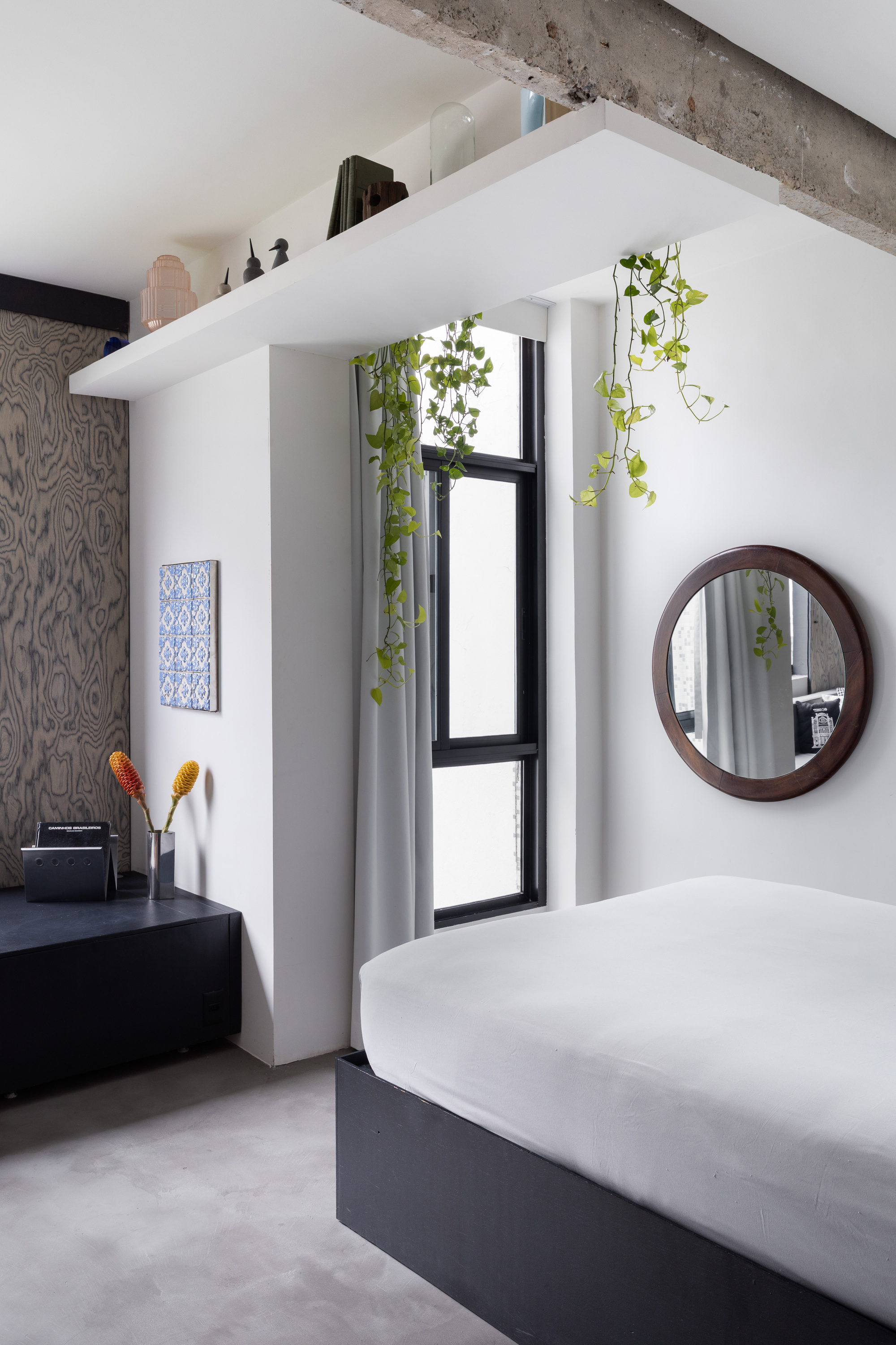 Bedroom corner showing black-framed window with trailing vines and round wooden mirror