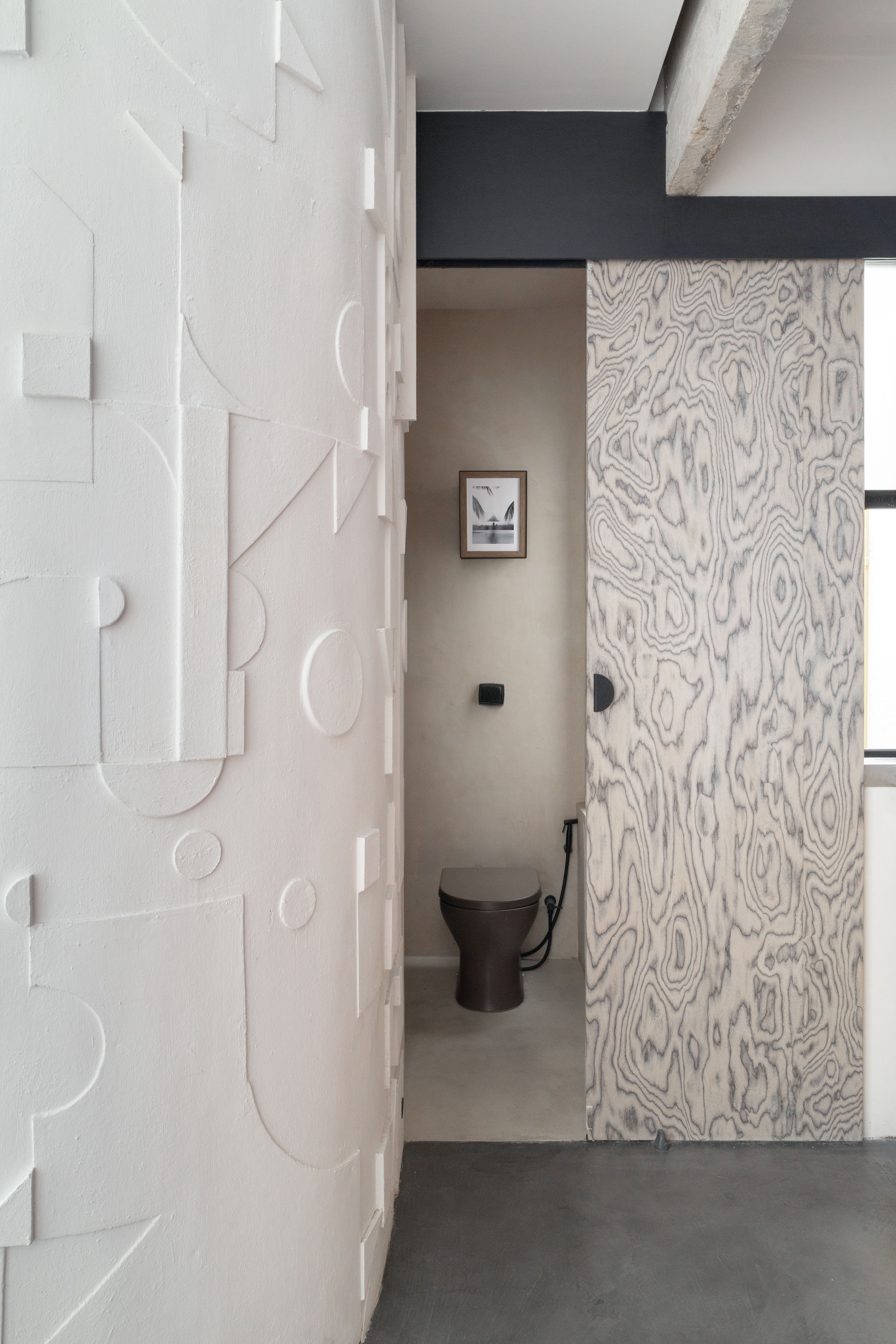 Bathroom entry through sliding wood grain door beside white geometric relief wall
