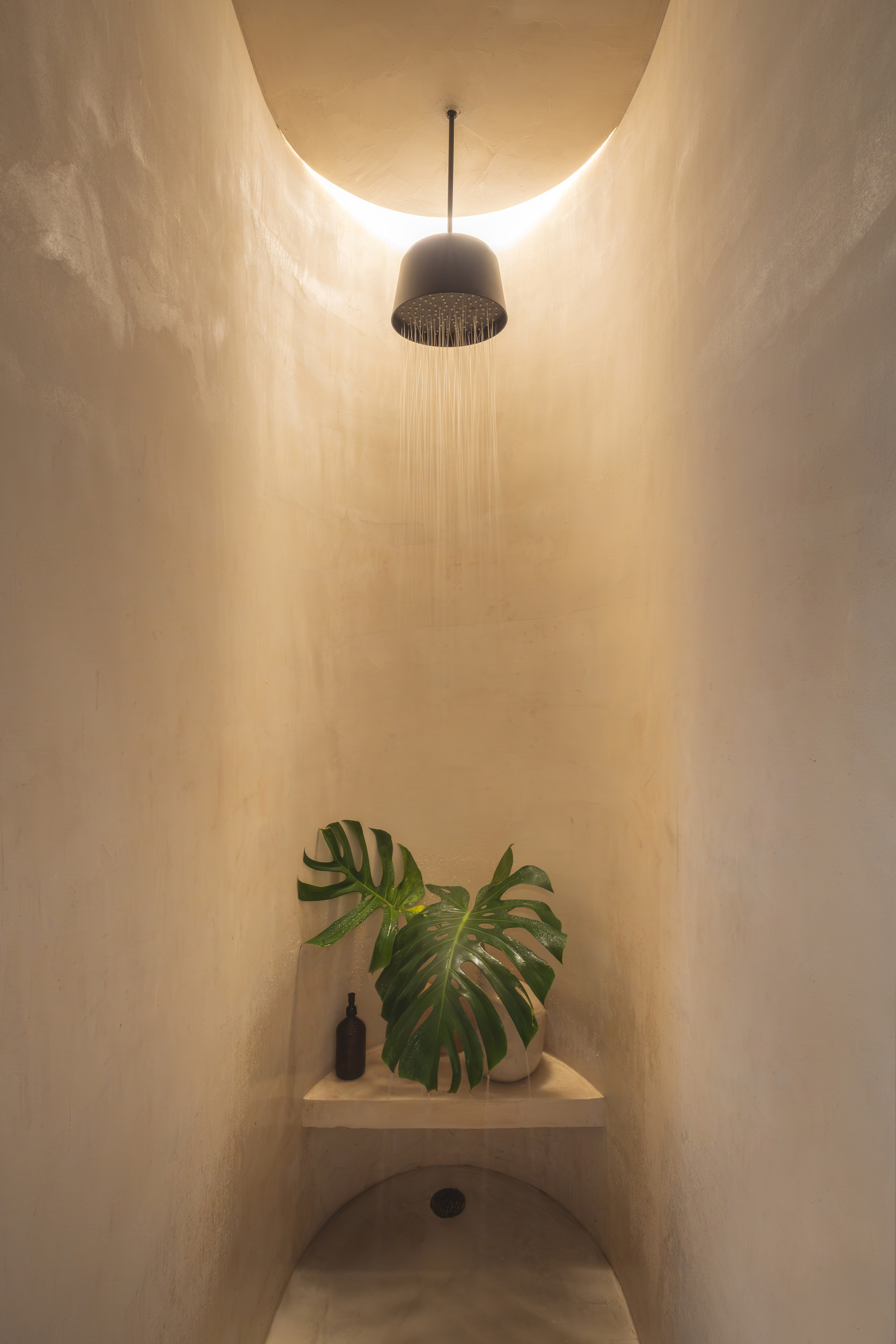 Illuminated shower alcove with water flowing from a perforated ceiling fixture at night