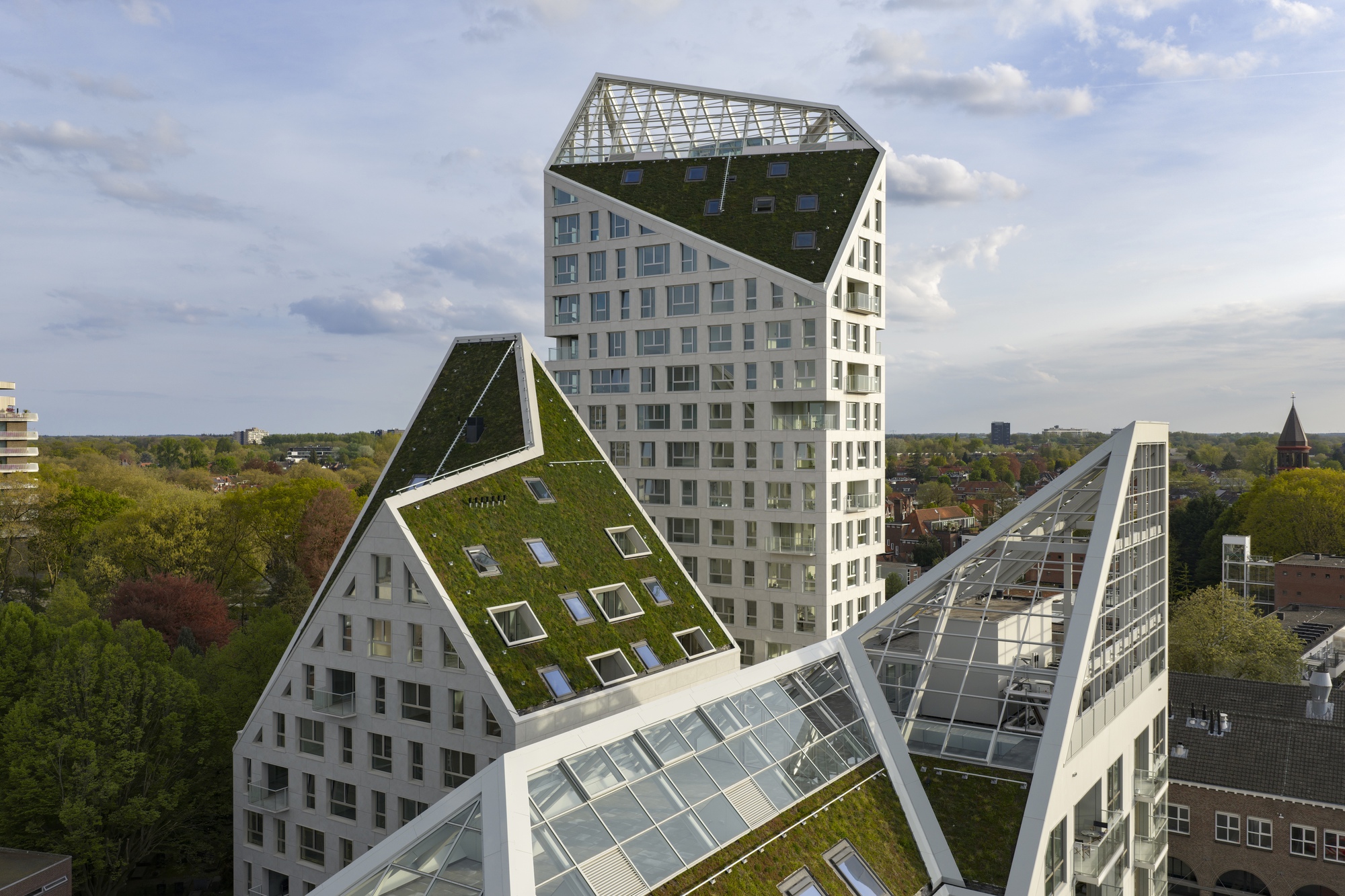 Aerial view of the clustered towers with planted and glazed gable roofs under partly cloudy skies