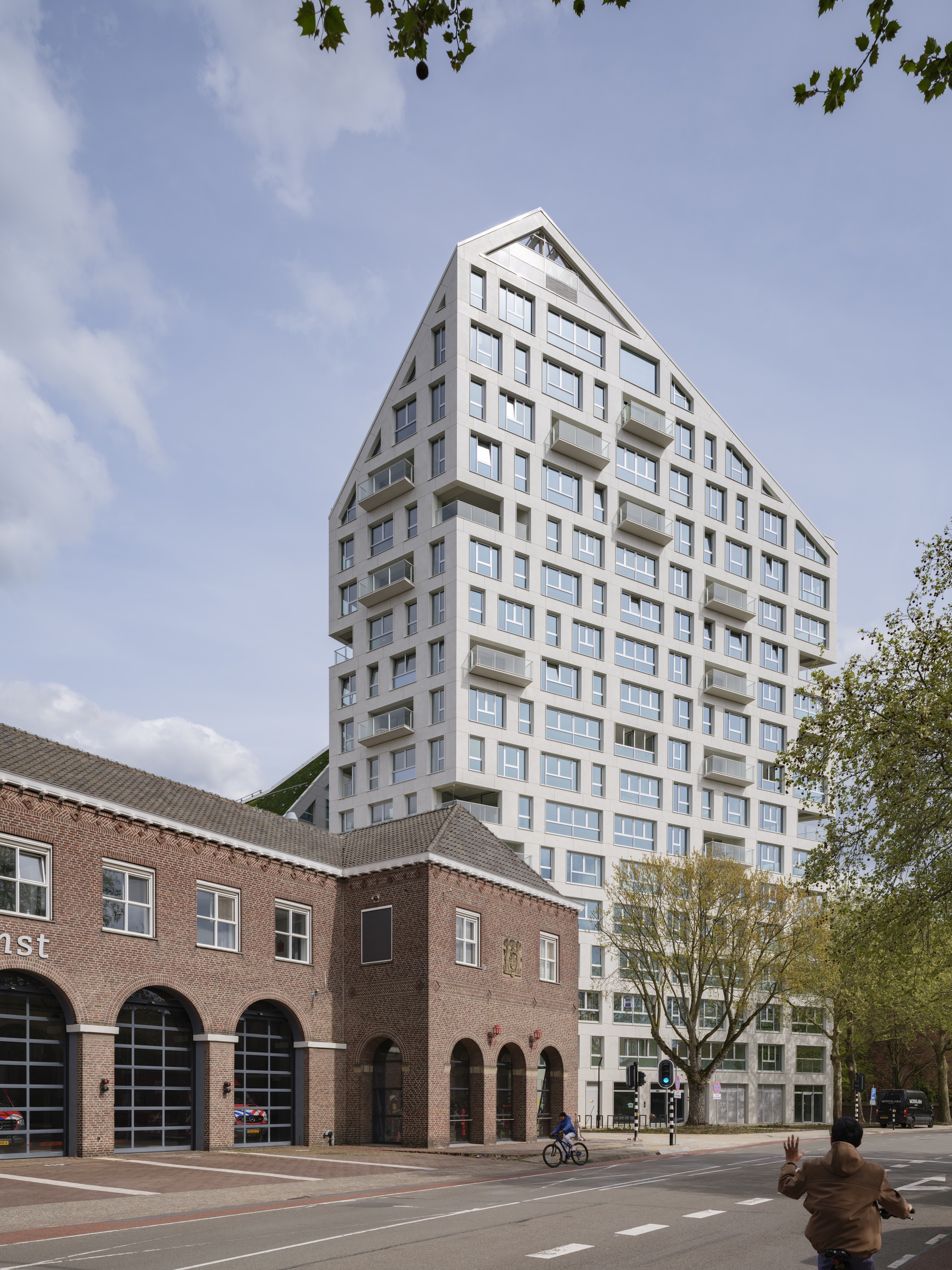 Street view of the white tower with recessed balconies rising above a historic brick arcade and a cyclist