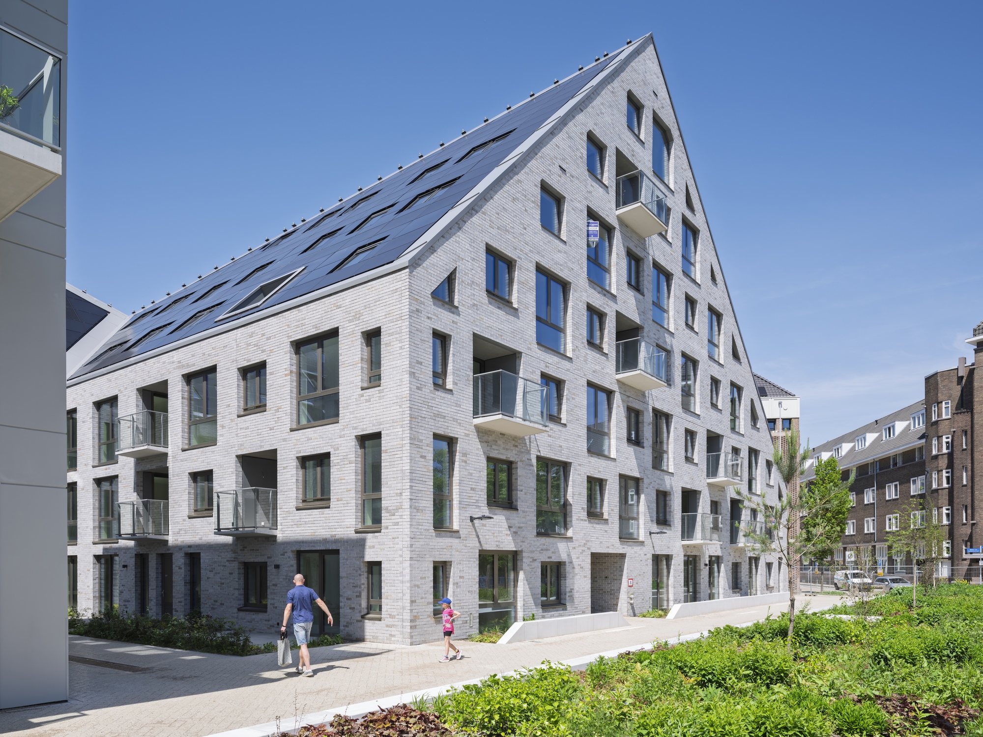 White brick residential facade with staggered balconies and residents walking on the sidewalk