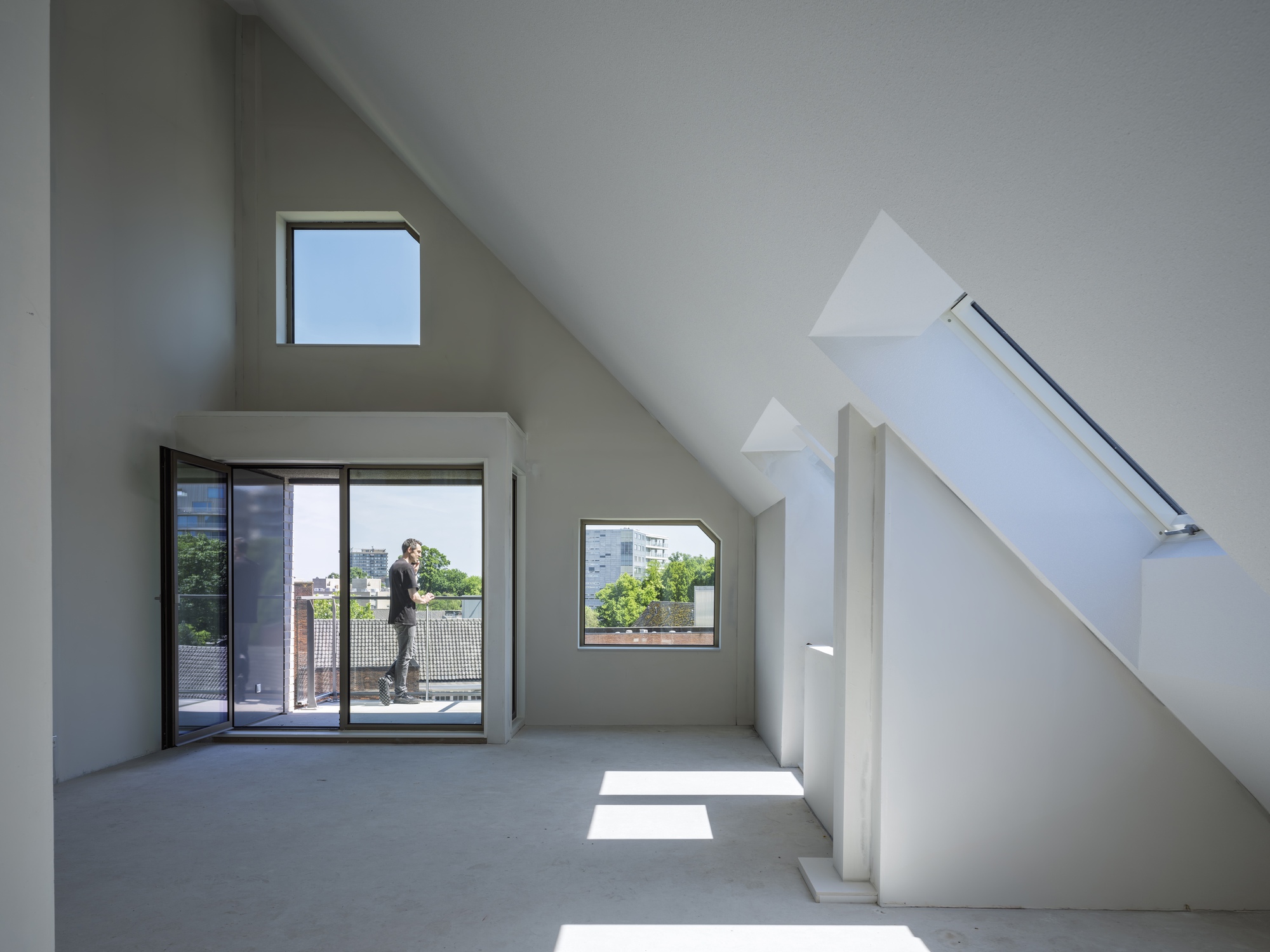 Interior attic space with sloped ceilings, multiple windows, and a figure on the balcony in afternoon light