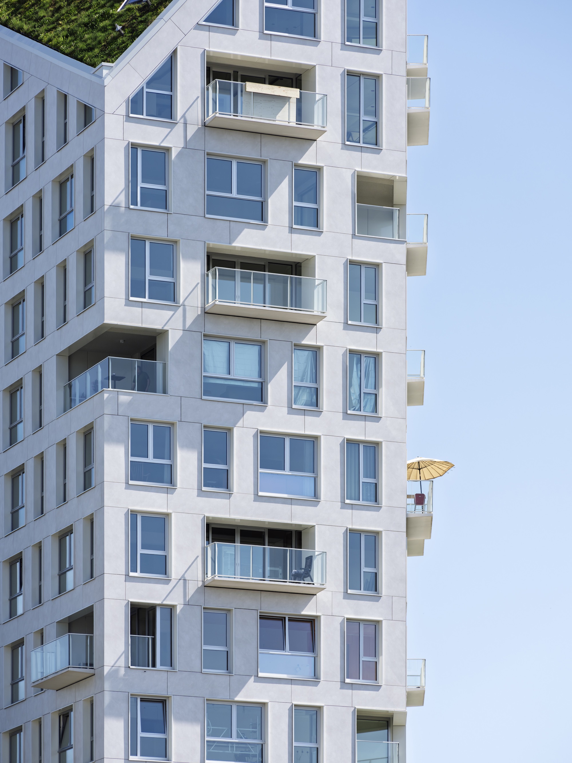 White facade with staggered balconies and glazed openings showing yellow umbrella on upper terrace