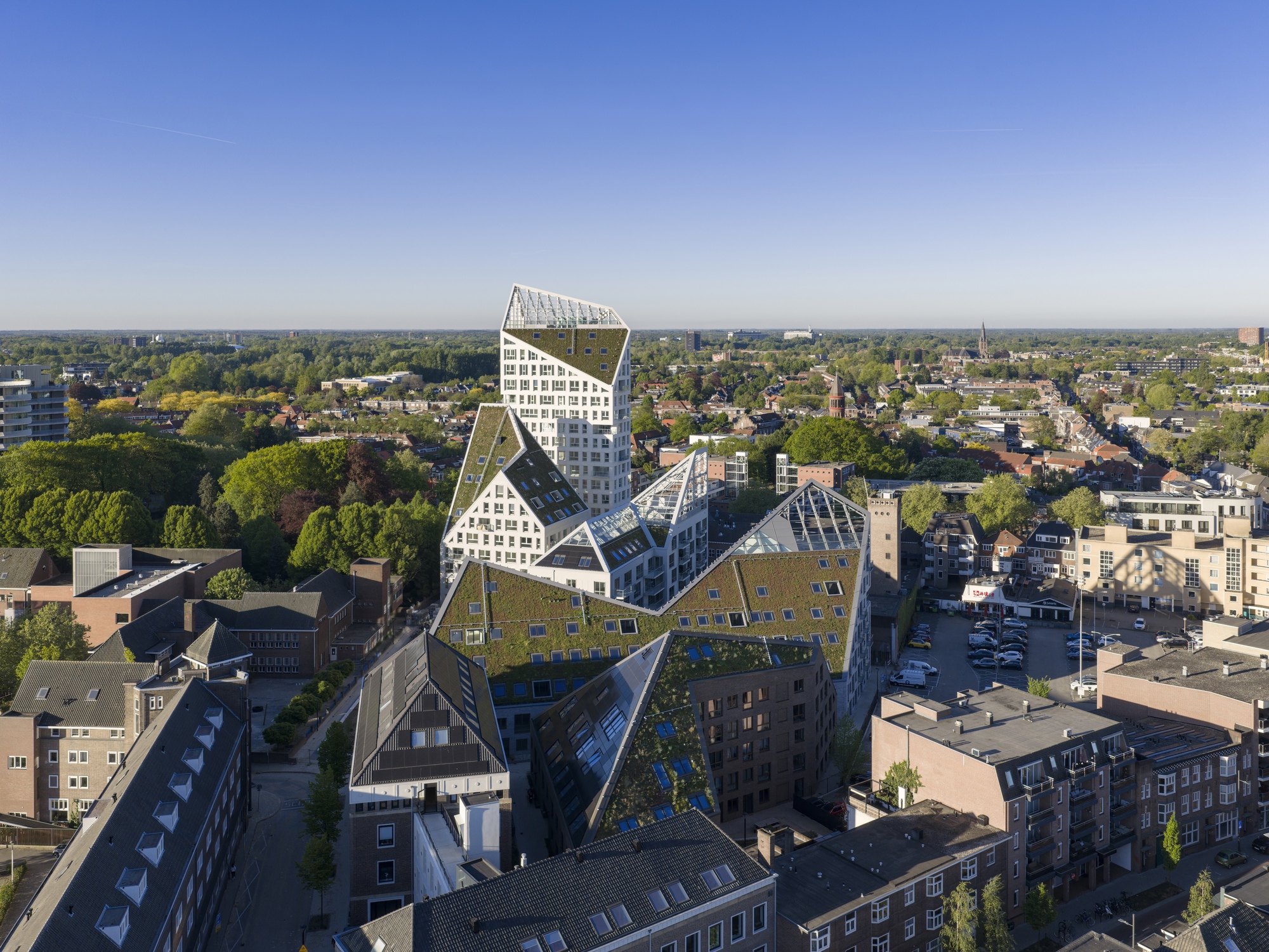 Aerial view of the zigzag pitched roof volumes with green roofs rising above low-rise urban blocks