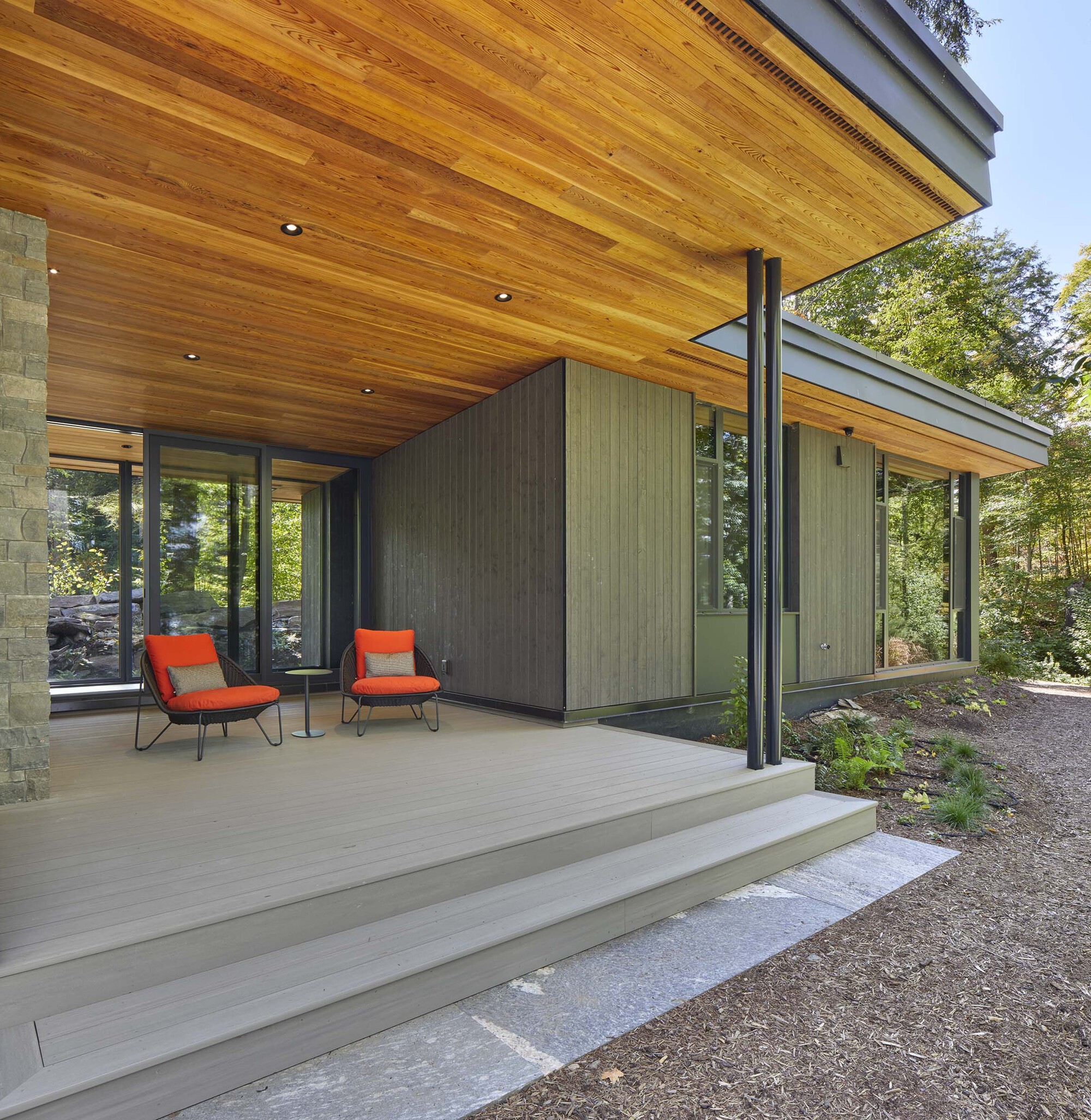 Covered terrace with timber ceiling, steel columns, and wooden deck steps descending to a gravel path