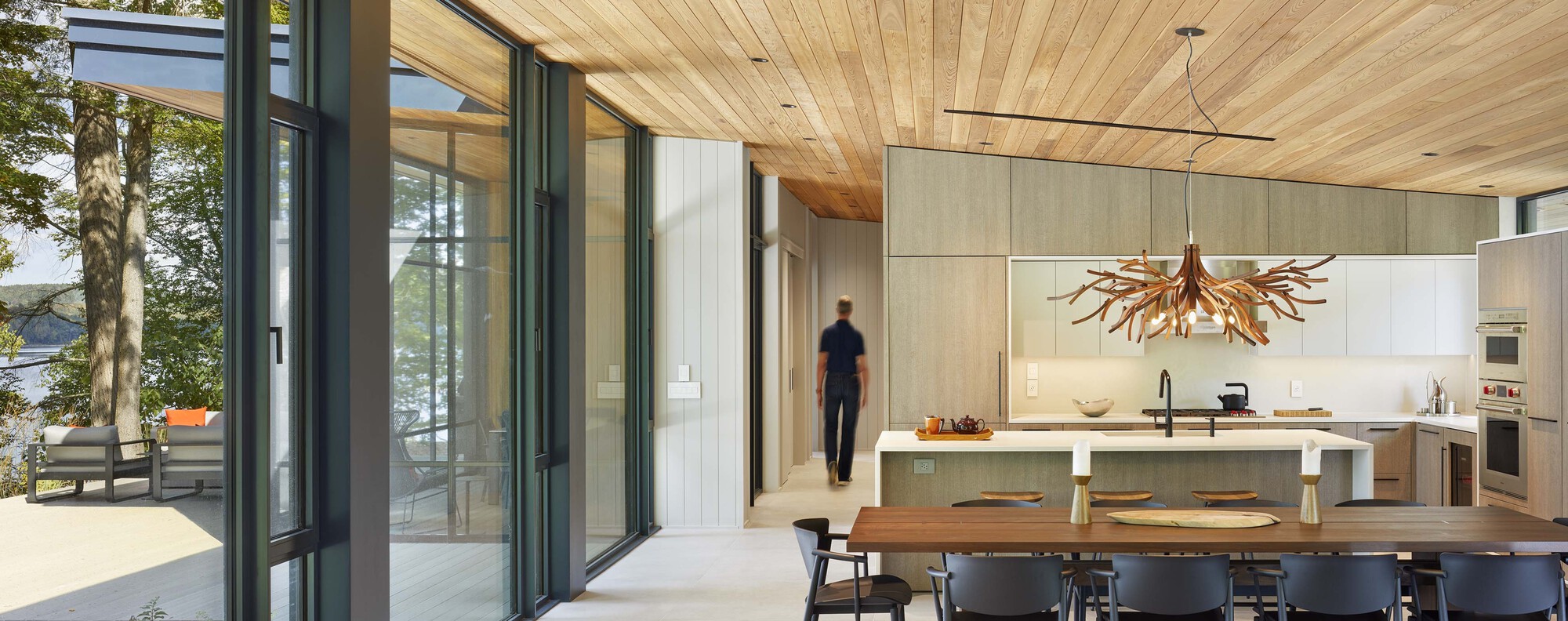 Kitchen island with extended dining counter under timber ceiling opening to glass-walled terrace beyond