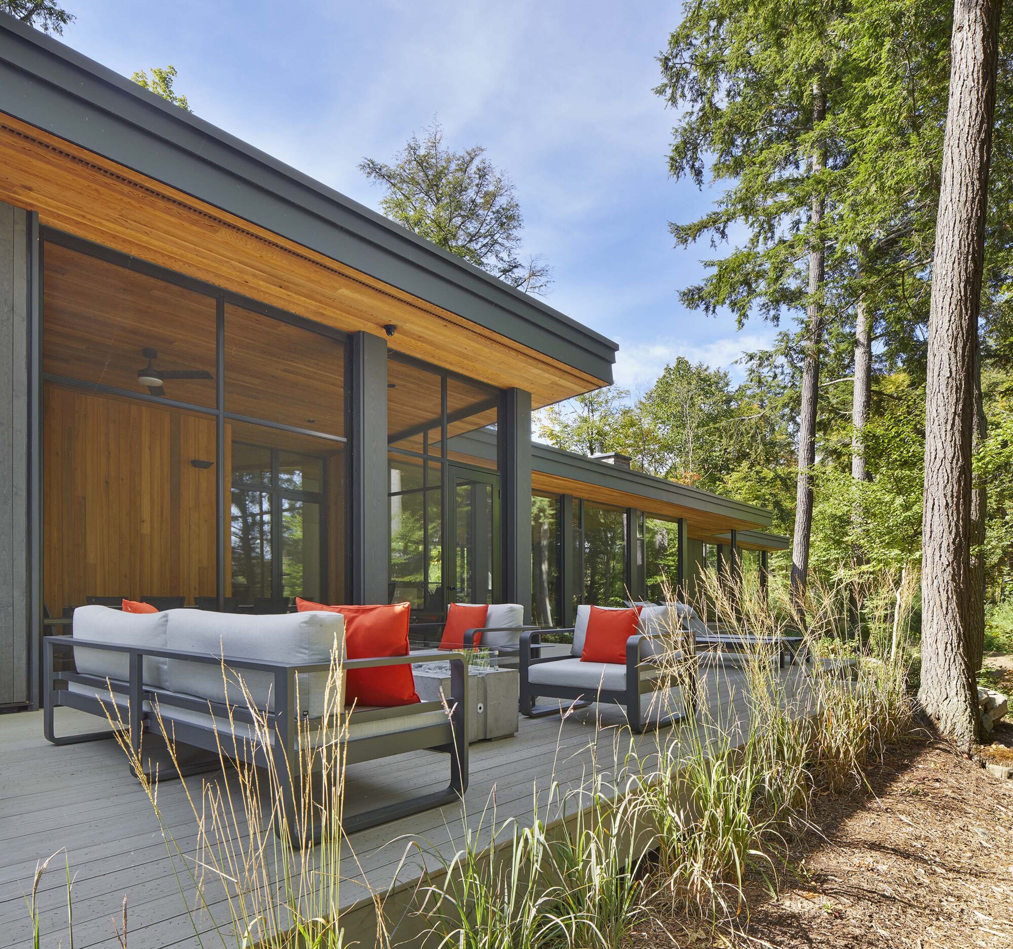 Outdoor terrace with seating adjacent to floor-to-ceiling glazing and timber soffits under a clear sky
