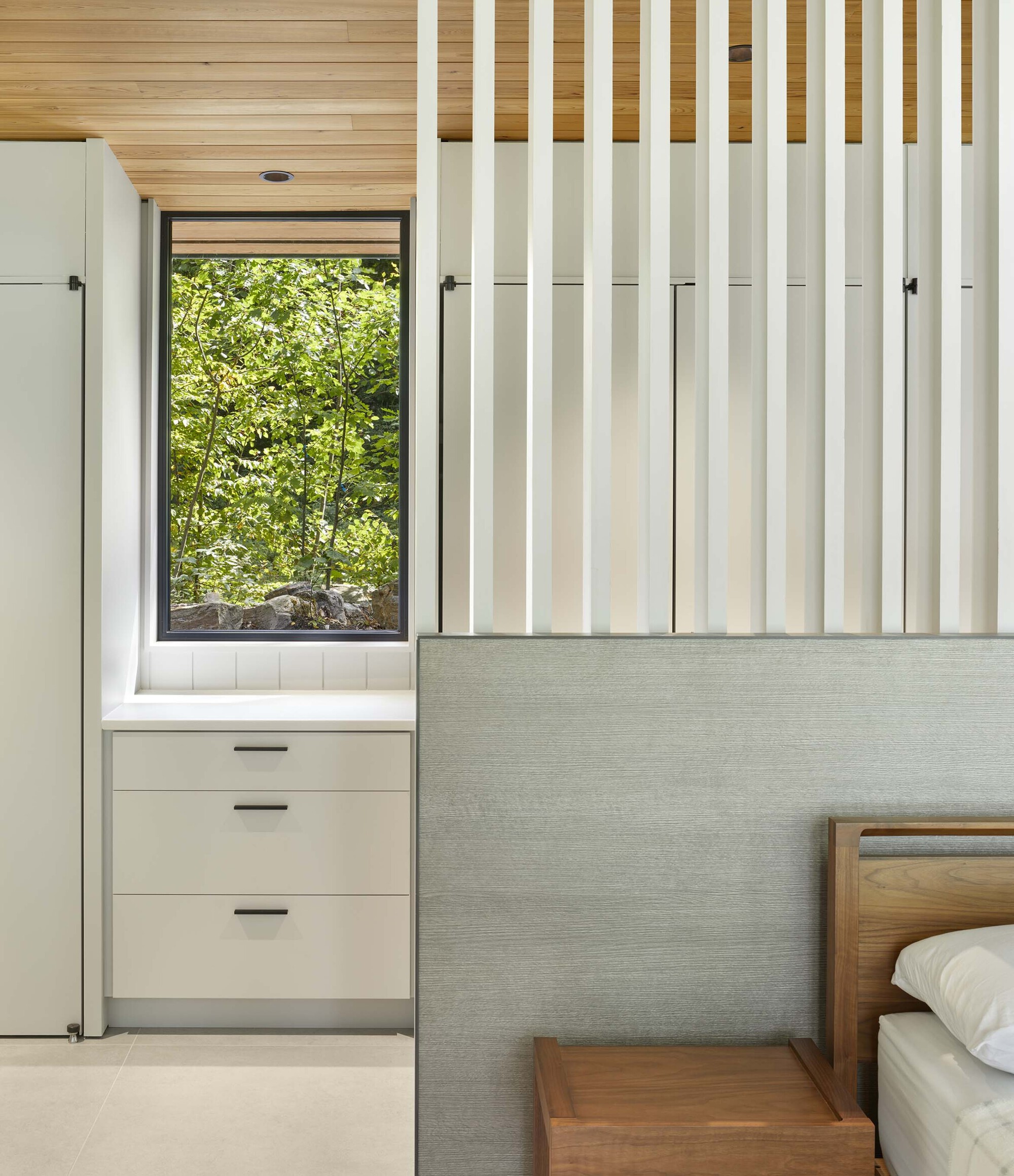 Built-in storage wall with vertical slat detail and window framing green foliage outside