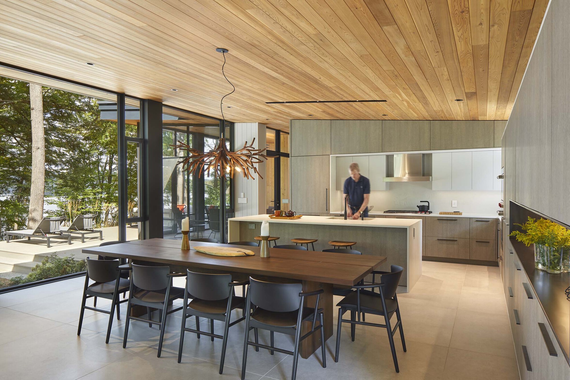 Open dining and kitchen space with timber ceiling and full-height glazing opening to lakefront terrace