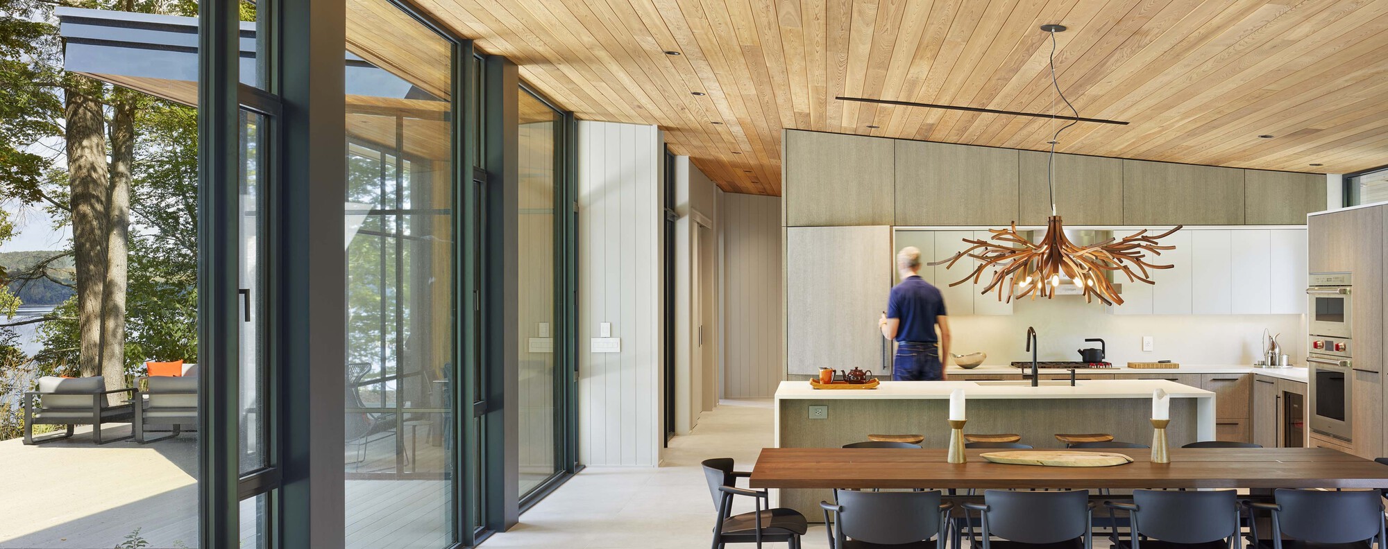 View from dining area through sliding glass doors to outdoor terrace with person moving through kitchen